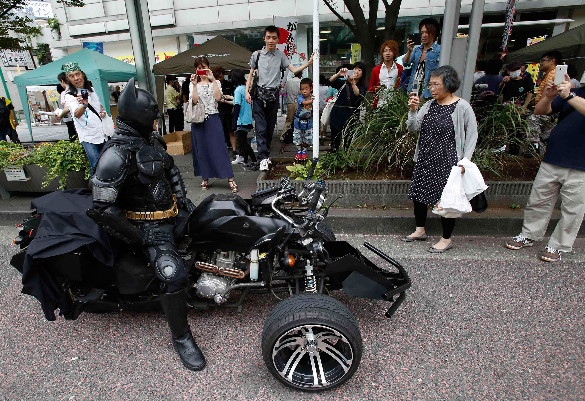 People take pictures of a 41-year-old man going by the name of Chibatman sitting on his "Chibatpod" in Chiba
