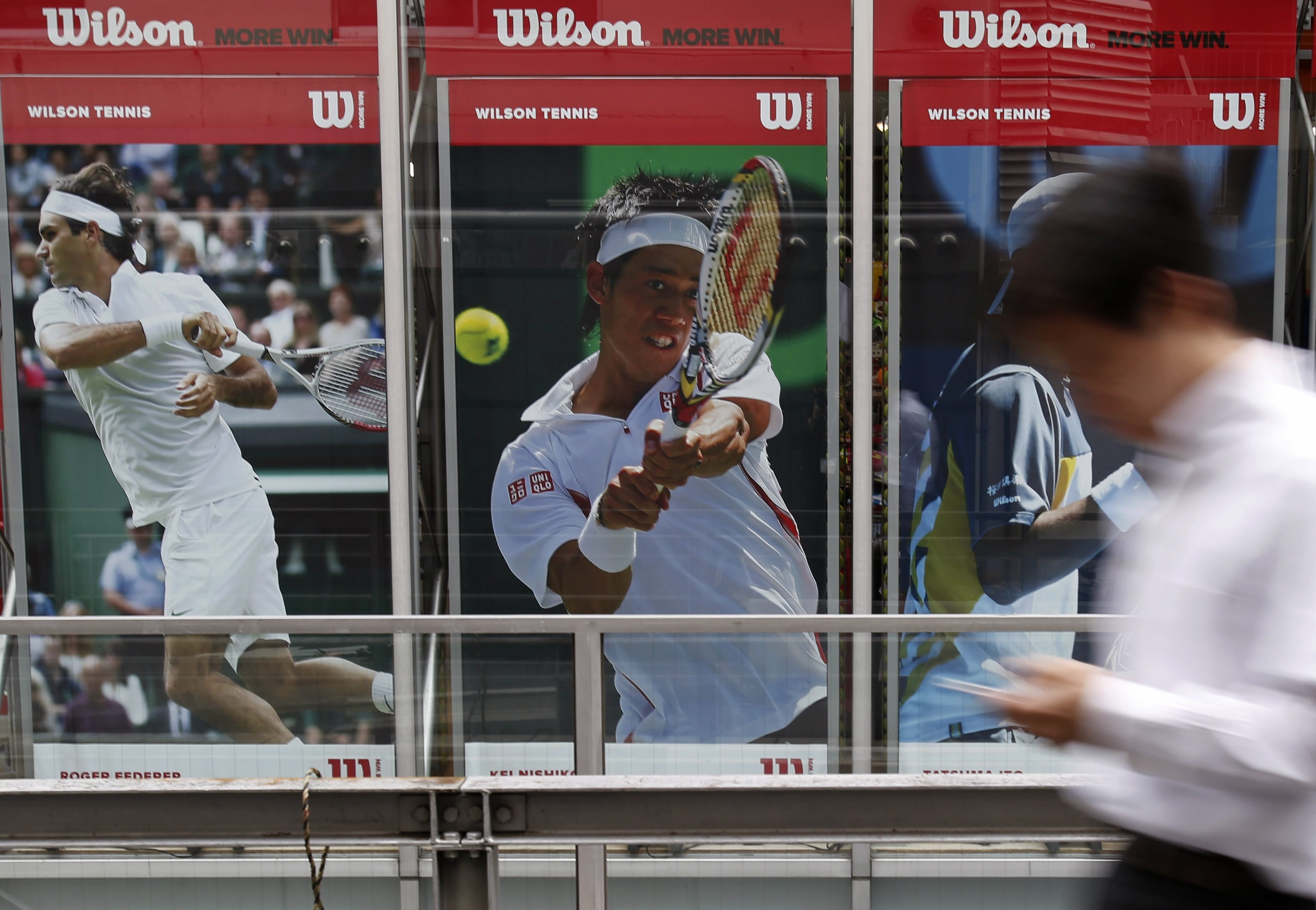 A man holding his mobile phone walks in front of a poster of tennis players Kei Nishikori of Japan (C) and Roger Federer of Switzerland (L) outside a sports shop in Tokyo on Sept. 8, 2014. Tenth seed Nishikori is the first Asian man to reach a grand slam singles final while his opponent, Croatia's Marin Cilic, is also into his first final.