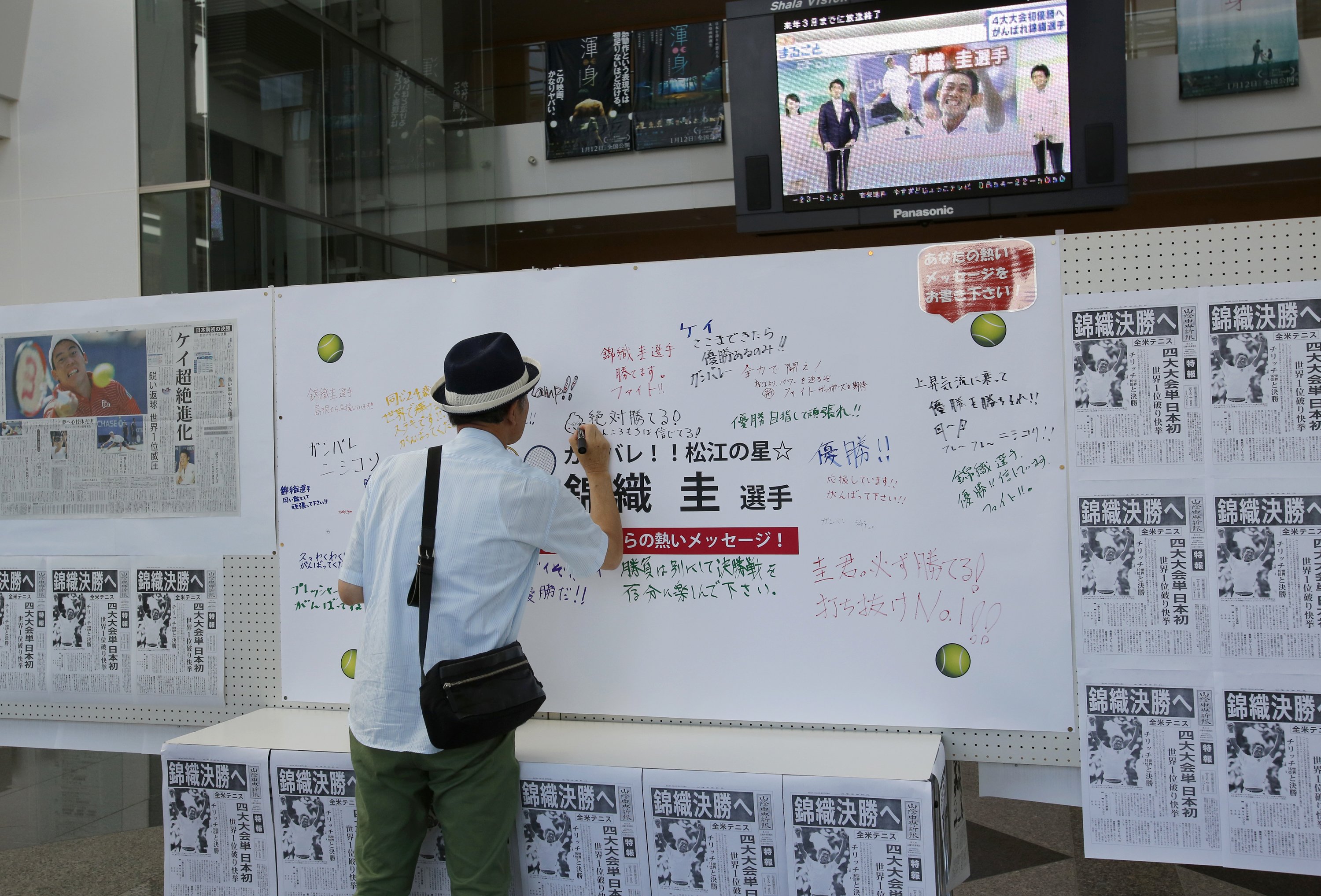 A man writes a message to Japanese tennis player Kei Nishikori on a board with newspapers reporting him in the U.S. Open, in Nishikori's hometown of Matsue, Japan on Sept. 8, 2014.