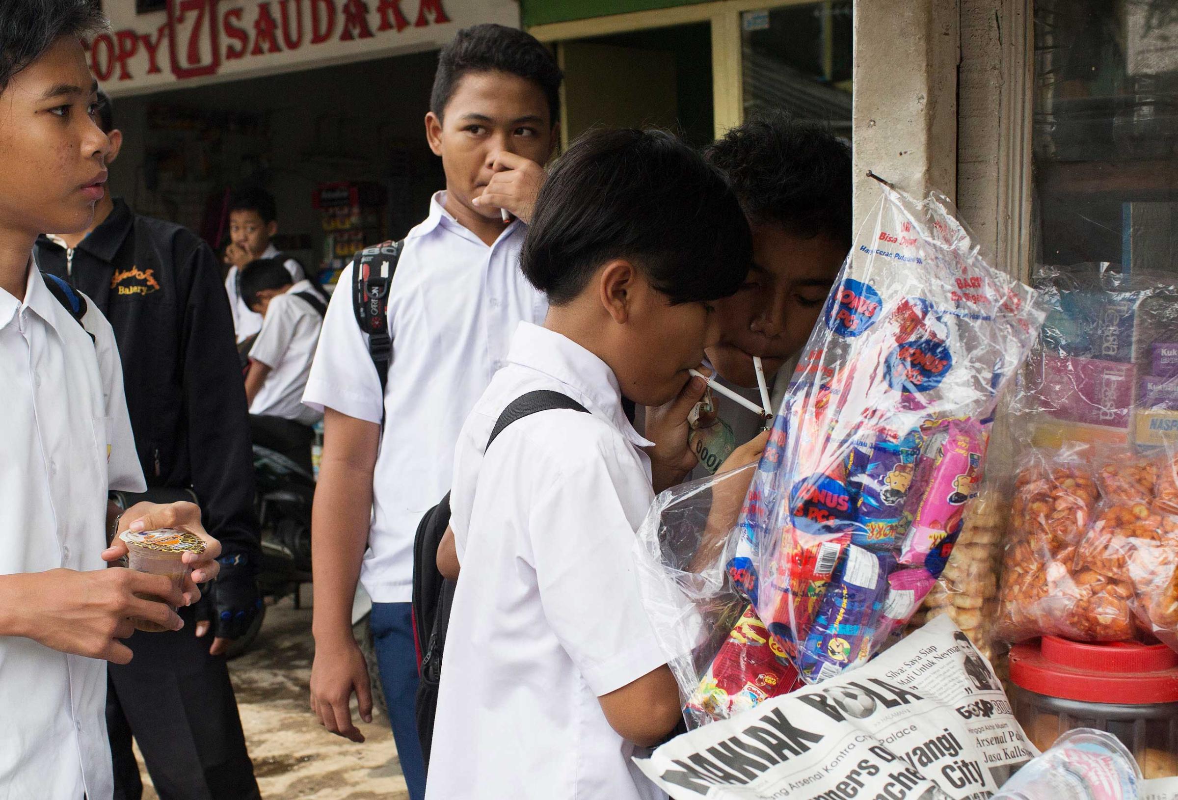 Groups of children buy single cigarettes and light them at a kiosk after school on February 12, 2014 in Jakarta, Indonesia. The children purchased cigarettes here without age identification and kiosks such as this one can be found near schools around the city.