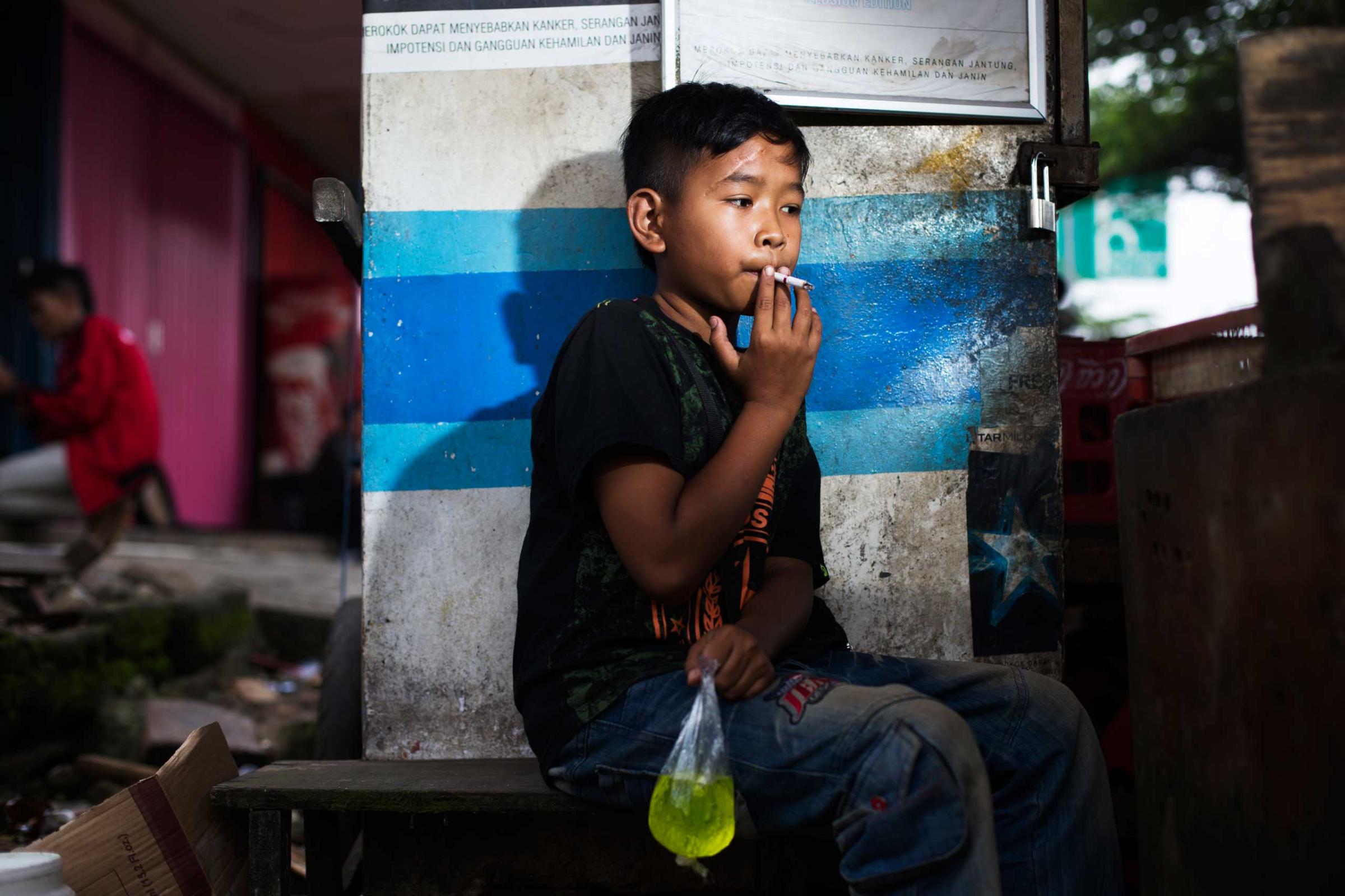 Eman poses for a photo as he smokes a cigarette while clutching a bag of juice in east Jakarta, Indonesia on February 12, 2014.