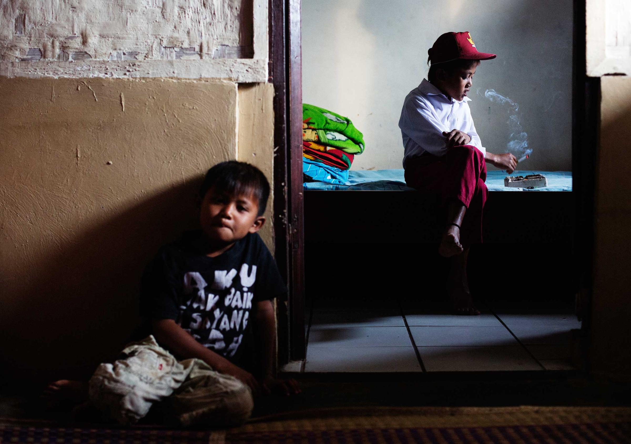 Ilham Hadi, who has smoked up to two packs a day and began when he was four years old, poses for a photo wearing his third grade uniform while smoking in his bedroom as his younger brother looks on in their village near the town of Sukabumi, Indonesia on February 14, 2014.