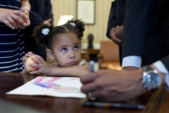 Luz Graham-Urquilla, 4, watches President Obama as he signs her drawing at the Resolute Desk in the Oval Office, May 25, 2012.
