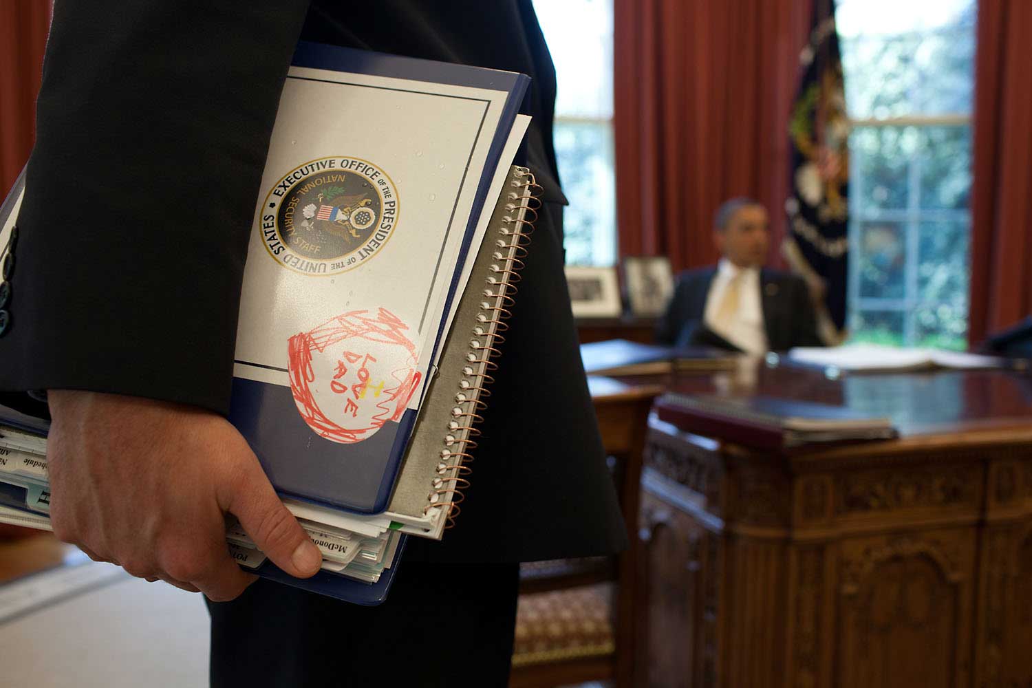 Denis McDonough, Deputy National Security Advisor, holds a binder with a note from his son as he and others brief President Obama in the Oval Office, March 29, 2012.