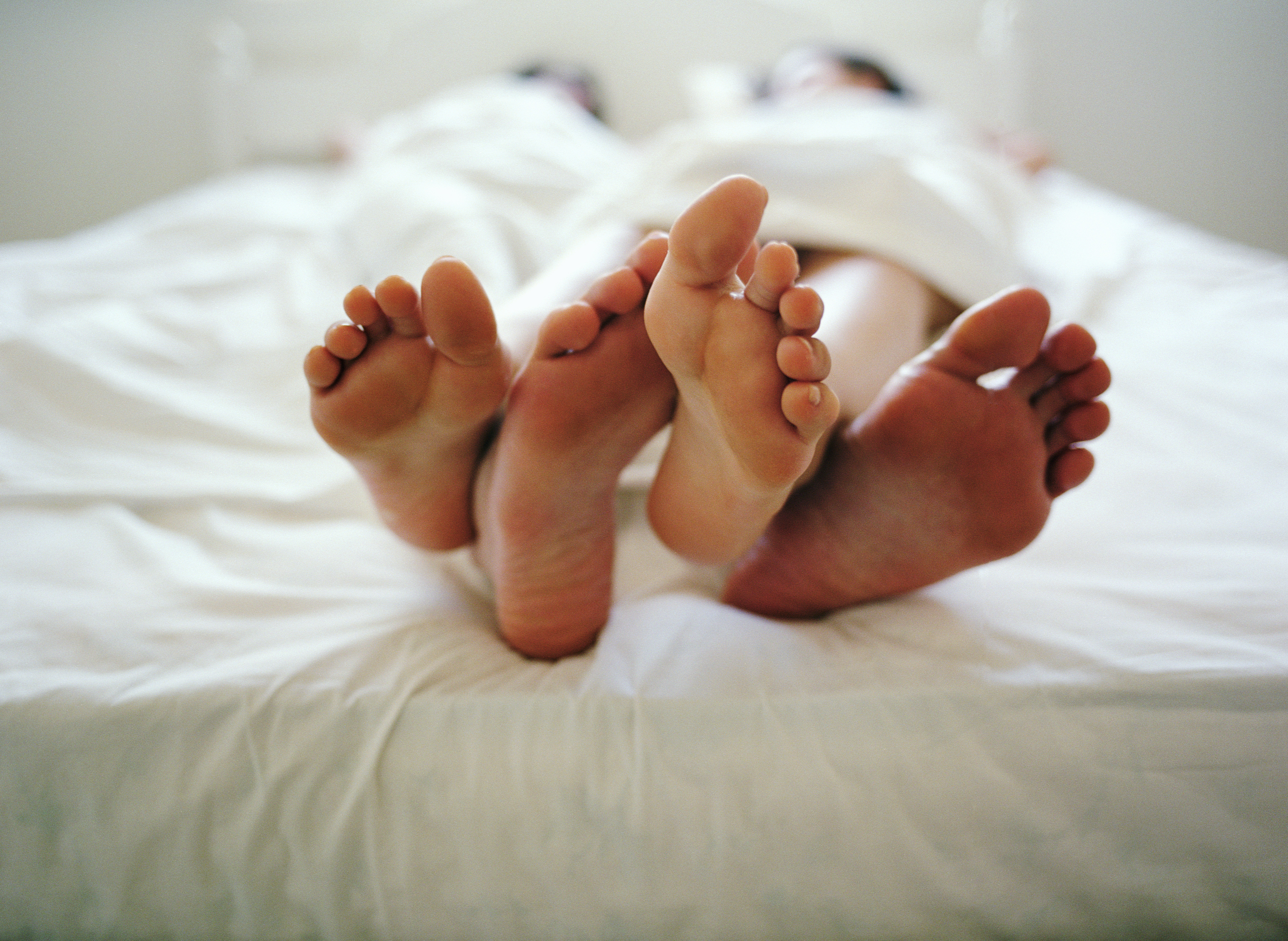 Young couple lying in bed under sheets, low section, close-up of feet