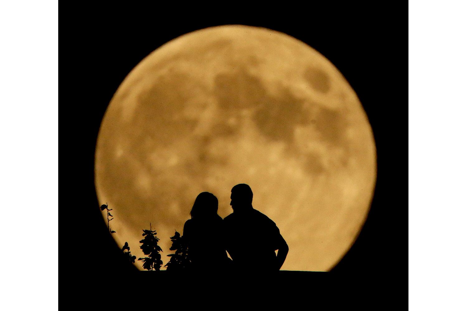 A couple sits on a bluff overlooking the Missouri River as the harvest supermoon rises in Kansas City, Mo., on Sept. 8, 2014.