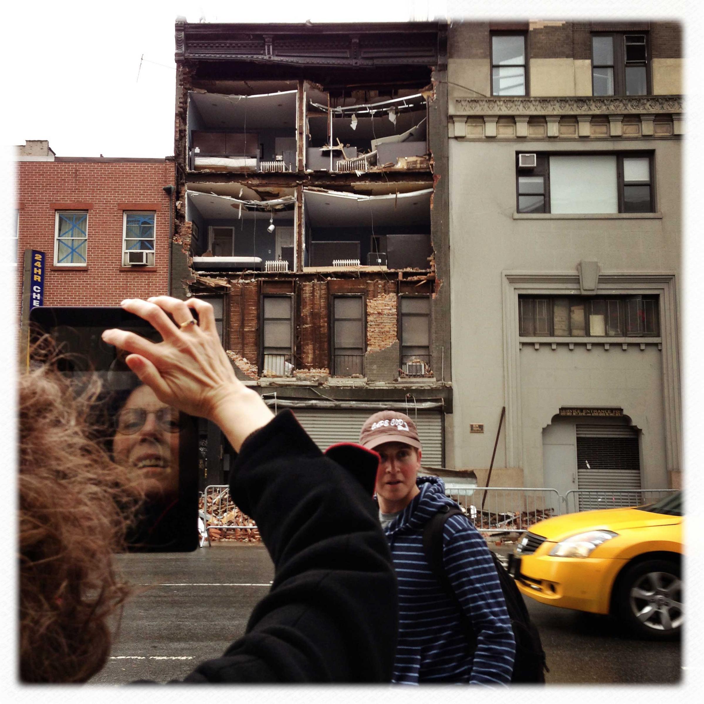A woman uses an iPad to photograph exposed bedrooms inside a building with a collapsed facade on 8th Avenue in Manhattan