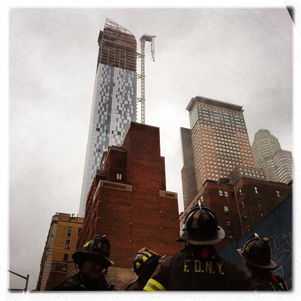 New York City firefighters look up at a crane dangling from a building on 57th Street, between Sixth and Seventh avenues, in Manhattan