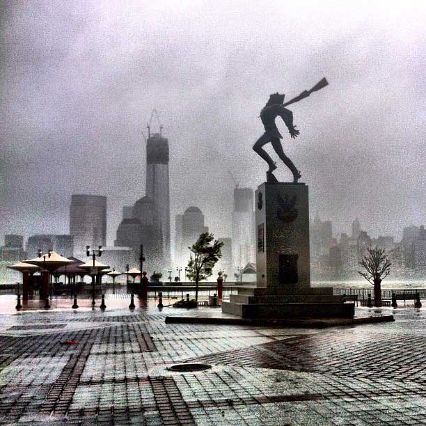 A statue braves the winds of Hurricane Sandy on the waterfront of Jersey City, N.J., with the unfinished World Trade Center looming over lower Manhattan
