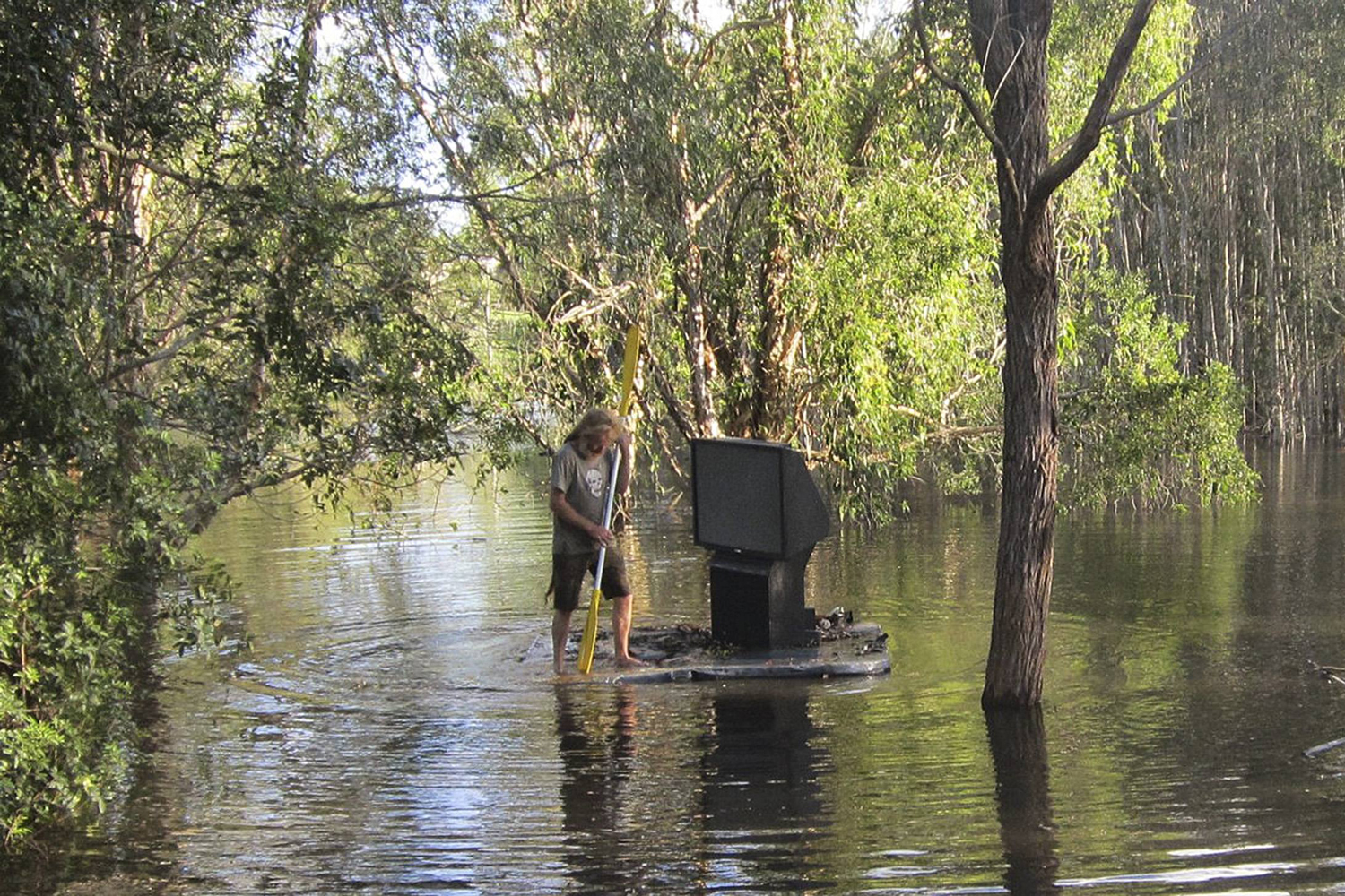 A man uses a spa cover to move a TV set through floodwaters at Cornubia