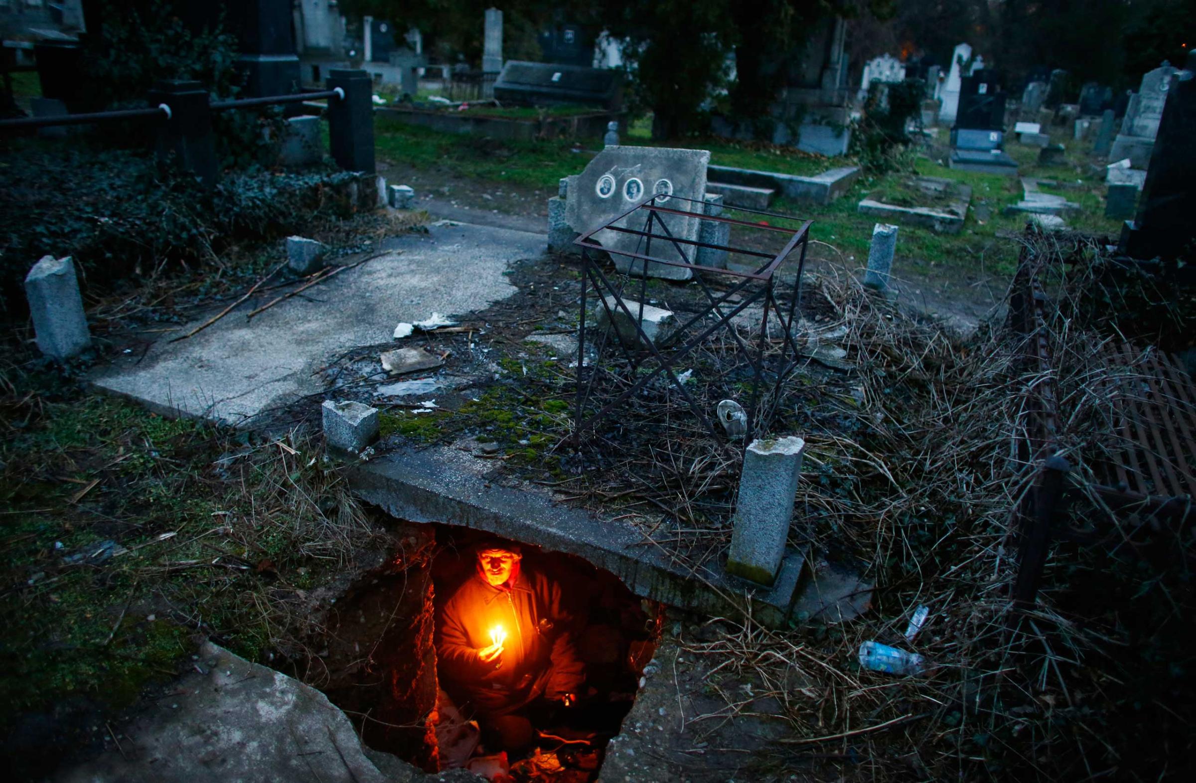 Bratislav Stojanovic, a homeless man, hold candles as he sits in a tomb where he lives in southern Serbian town of Nis