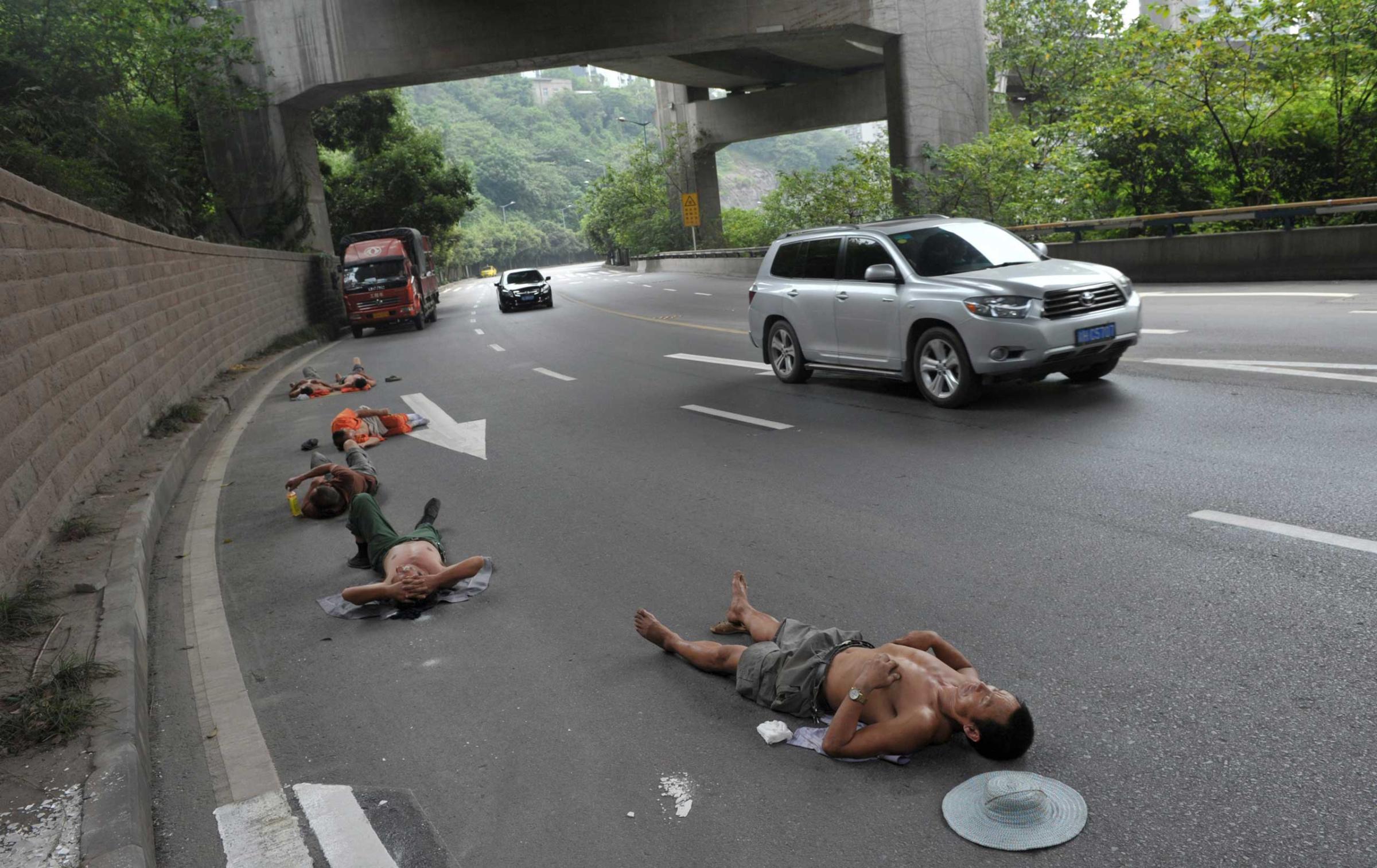 Labourers who work nearby nap on a road as cars drive past in Chongqing Municipality