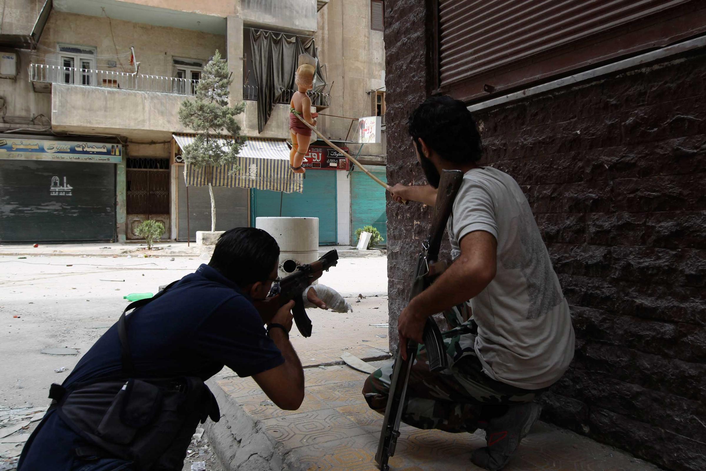 A Kurdish Free Syrian Army fighter holds doll while his fellow fighter takes shooting position in Ashrafieh, Aleppo