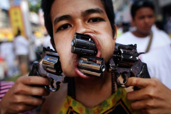 A devotee, with two guns pierced through his cheeks, takes part in a street procession during the annual vegetarian festival in Phuket