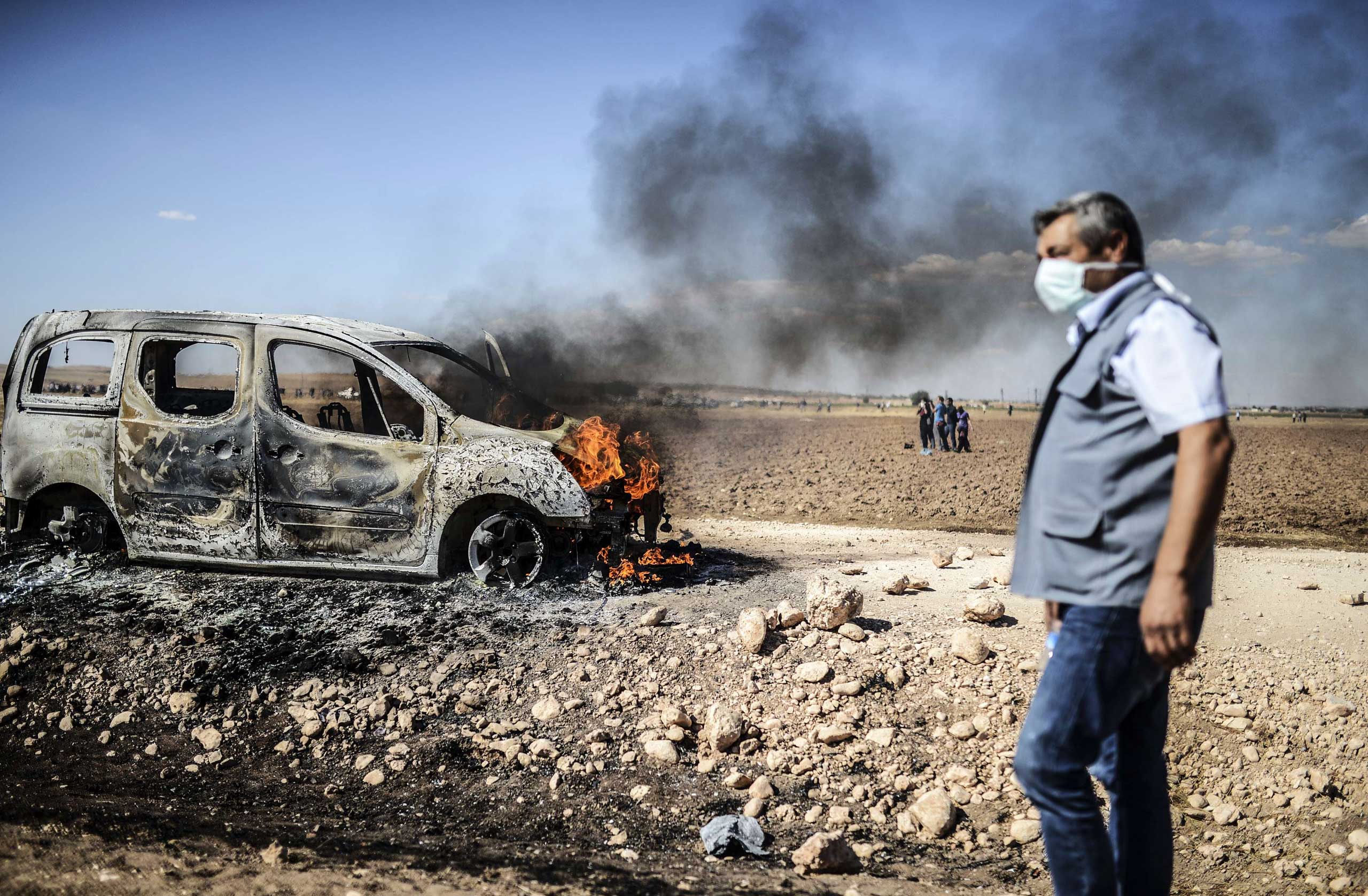 A man walks past a burning car as Kurdish protestors clashed with Turkish soldiers near the Syrian border after Turkish authorities temporarily closed the border at the southeastern town of Suruc in Sanliurfa province, on Sept.  22, 2014.