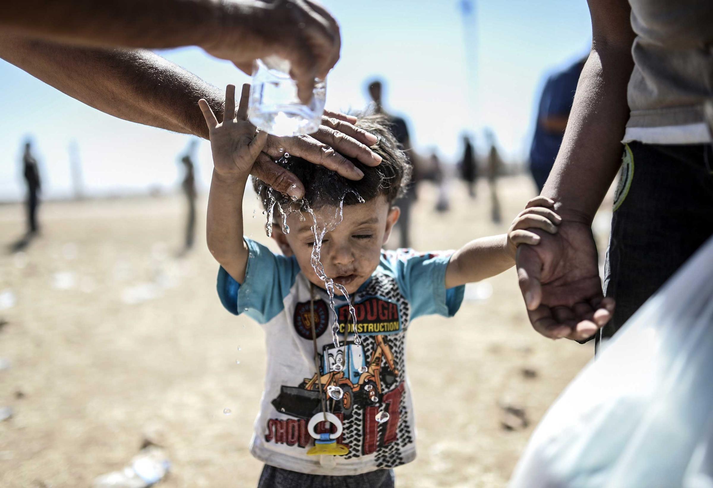 A Syrian Kurd pours water on a child after they crossed the border between Syria andTurkey near the southeastern town of Suruc in Sanliurfa province, on Sept. 20, 2014.