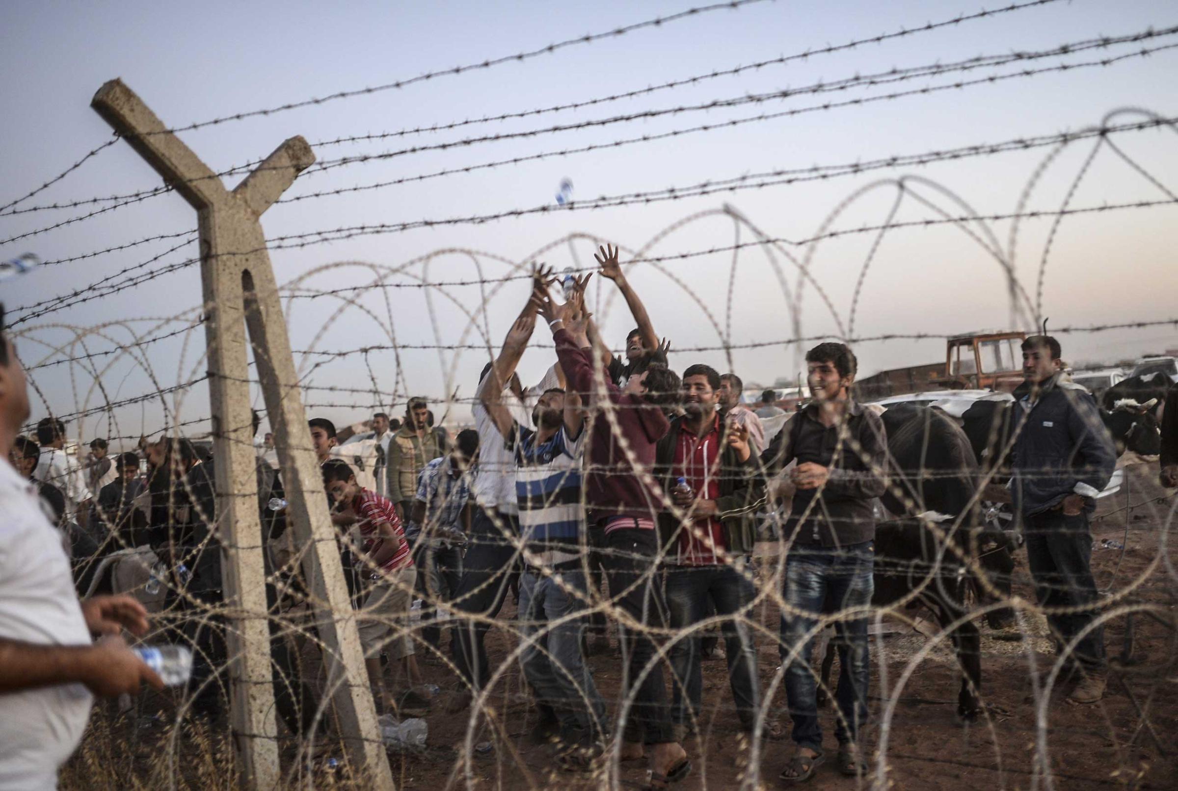 Syrian Kurds try to grab water thrown from Turkey near the border with Syria as they wait to take care of their animals at the southeastern town of Suruc in Sanliurfa province, on Sept. 21, 2014.