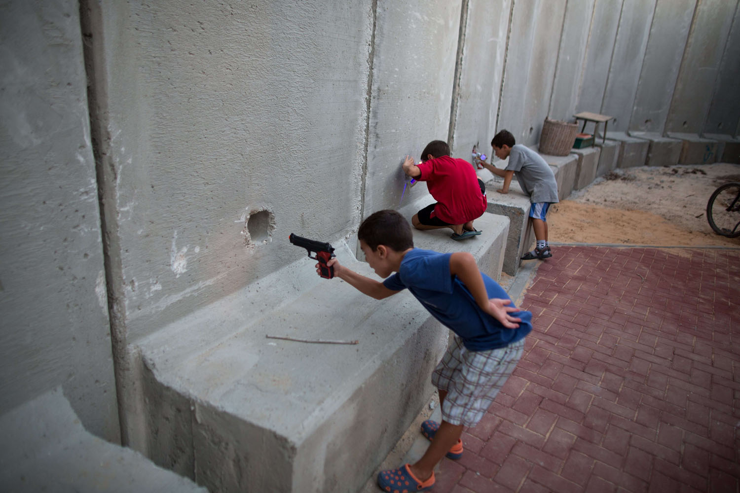 Sept. 9, 2014. Israeli children hold toy guns as they pretend to play war games next to newly built protection cement walls around a kindergarten in the center of Kibbutz Nahal Oz located near the border with Gaza Strip. Since the ceasefire between Israel and Hamas following fifty days of fight most of Israeli residents leaving near the Gaza Border hace returned to their homes with high army alert and new measures to protect them.