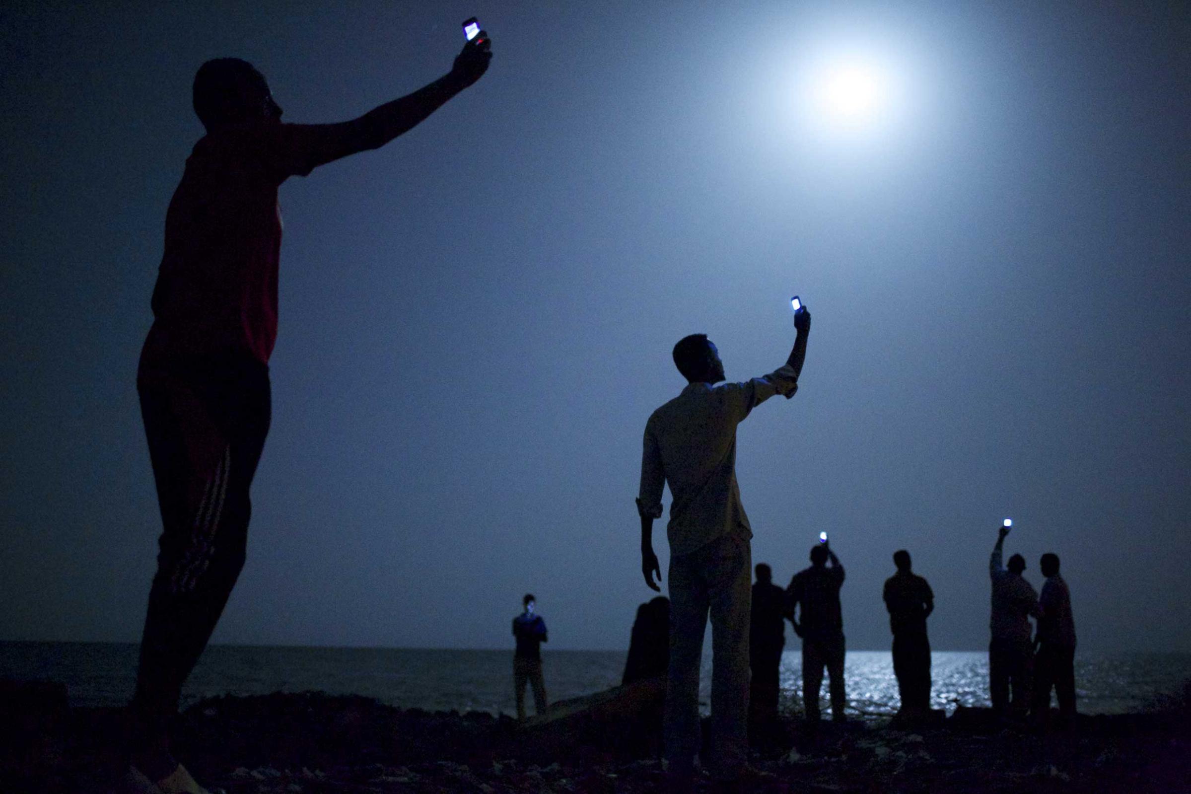 World Press Photo of the Year 2013.26 February 2013, Djibouti City, Djibouti. African migrants on the shore of Djibouti city at night, raising their phones in an attempt to capture an inexpensive signal from neighboring SomaliaÑa tenuous link to relatives abroad. Djibouti is a common stop-off point for migrants in transit from such countries as Somalia, Ethiopia and Eritrea, seeking a better life in Europe and the Middle East.