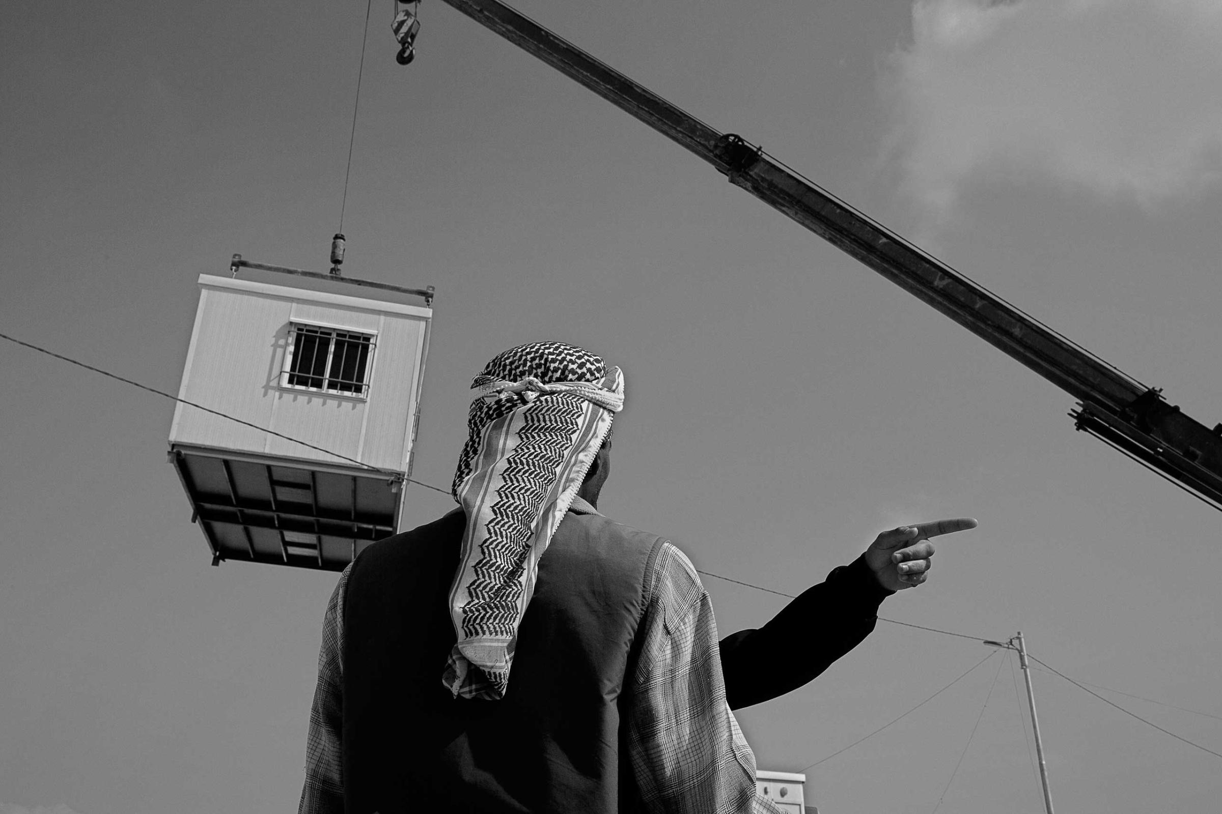 December 2013. Za'atari refugee camp, Jordan. A Syrian refugee watches a prefabricated unit being delivered to replace makeshift tents.