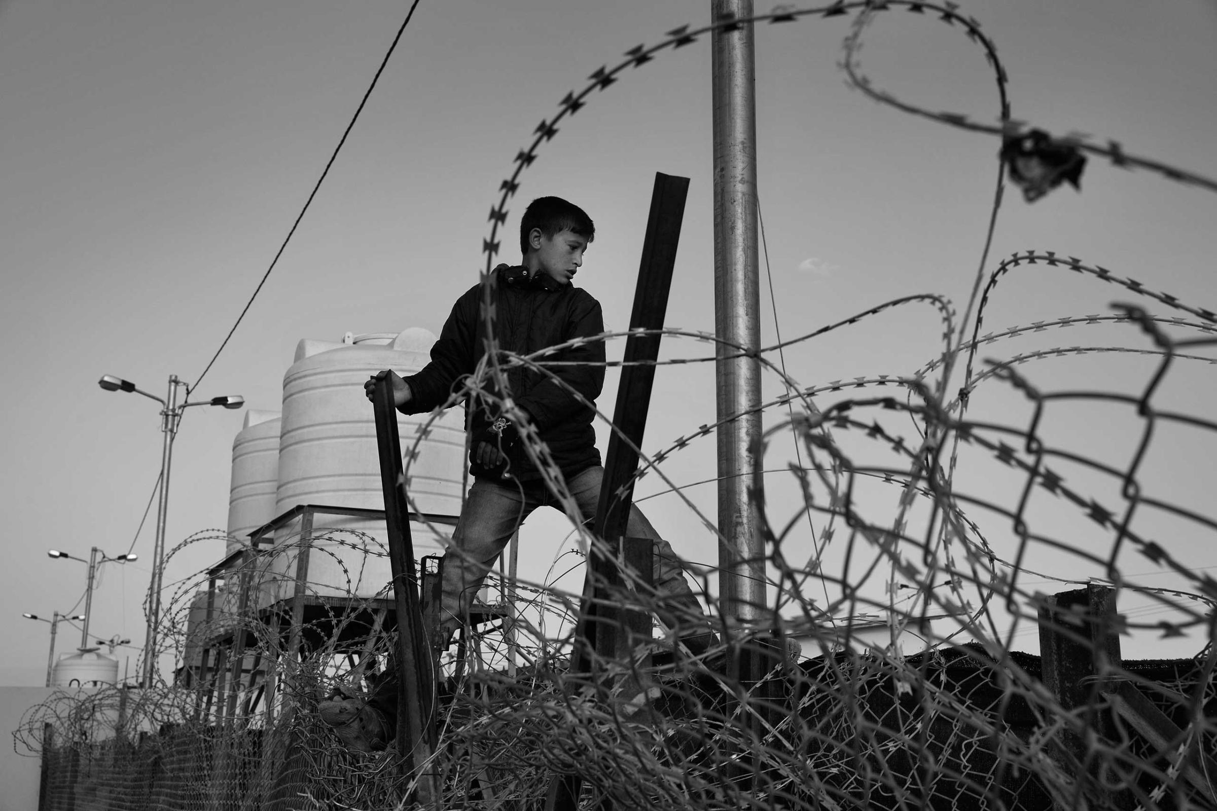 December 2013. Za'atari refugee camp, Jordan. Boys climb the fences to reach the newly arrived refugees and sell them bread, cigarettes and tea.