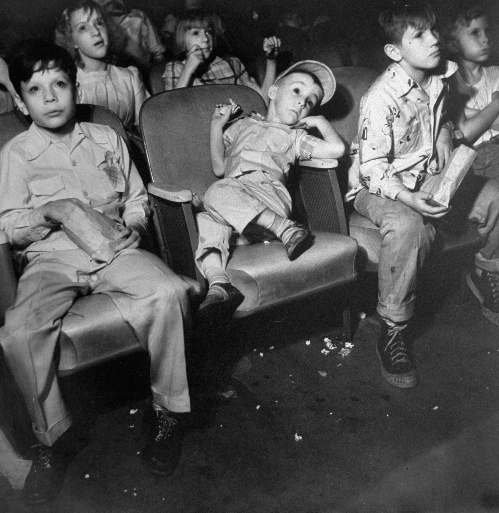 Kids shove popcorn into their mouths while keeping their eyes on the screen at the local movie house, Fresno, Calif., 1949.
