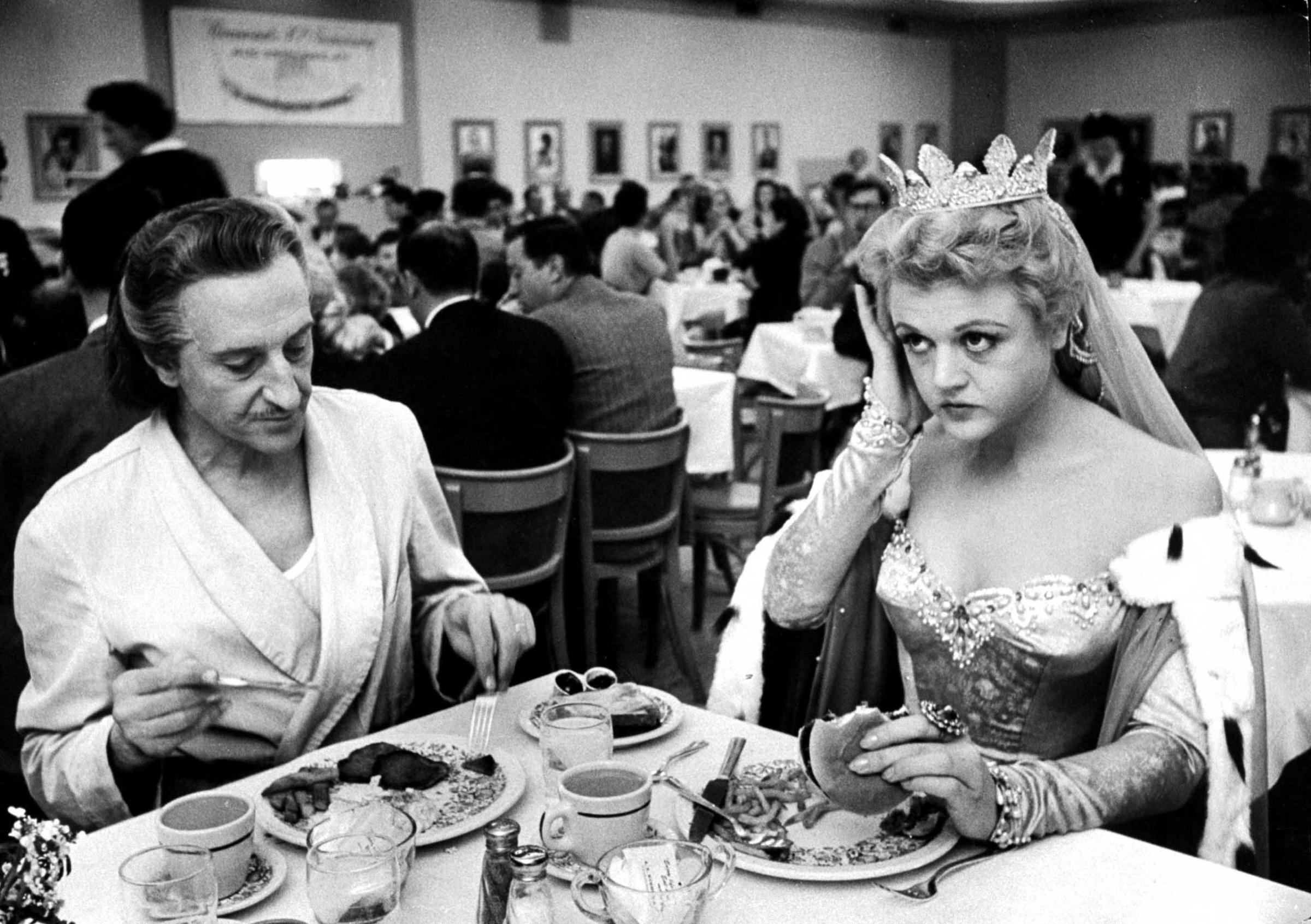Angela Lansbury, in costume for her role in The Court Jester, eats lunch with Basil Rathbone in the Paramount Studio commissary, December 1954.