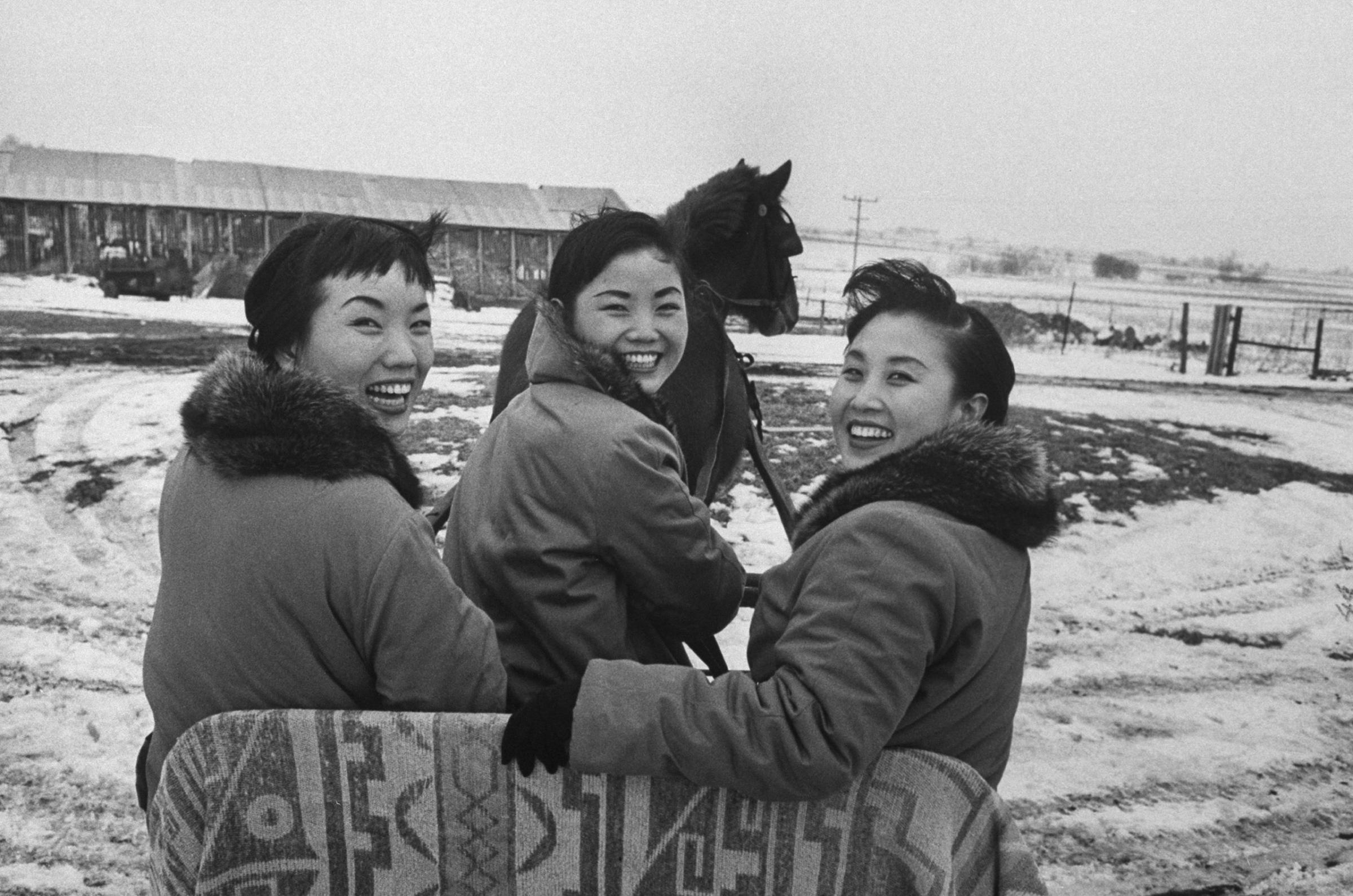 "On a sleigh, the three Kim sisters start off for a horse-drawn tour of [their manager's mother's] snow-covered Illinois farm. From the left are Sook Ja, Ai Ja, and Min Ja."
