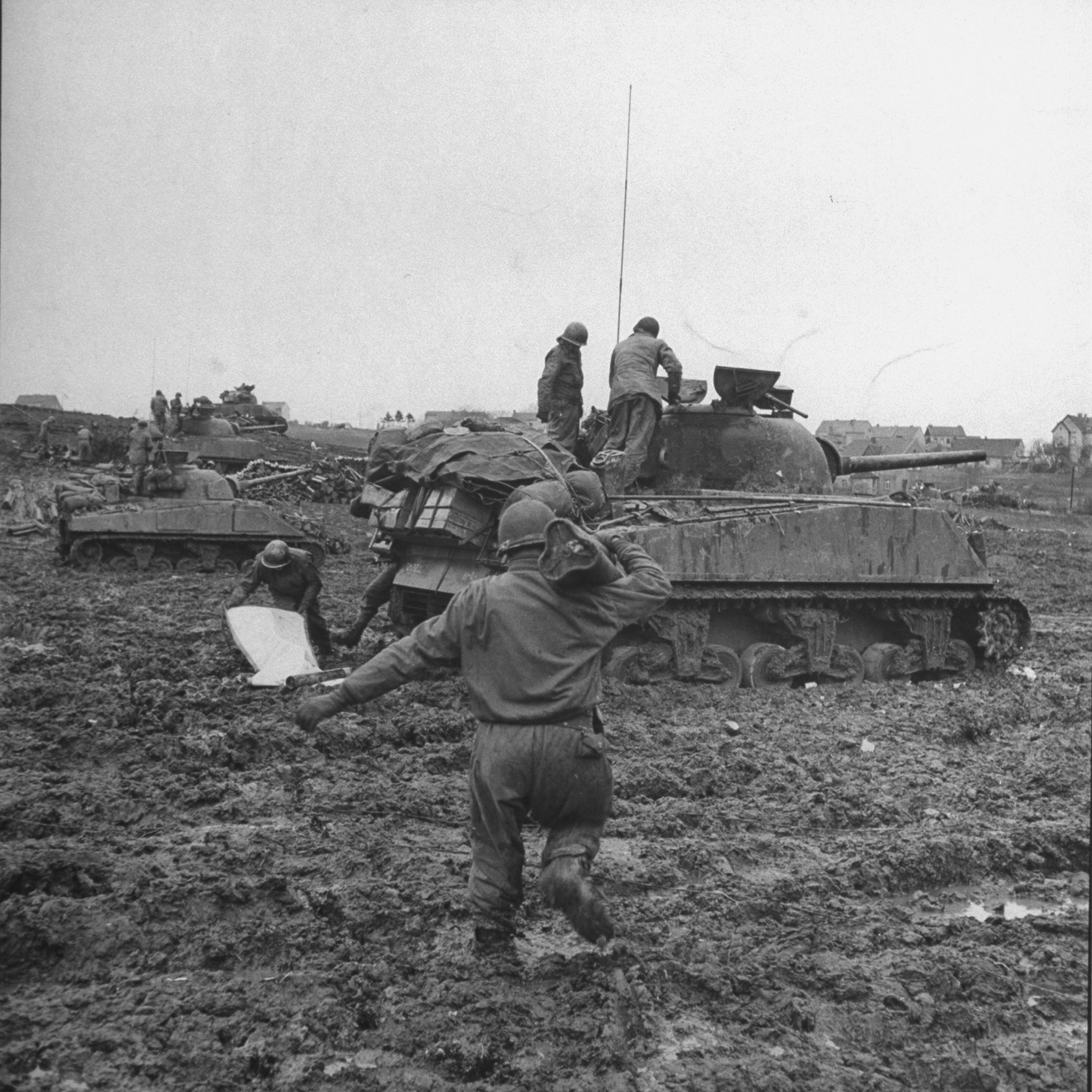 An American soldier slogs through deep mud carrying ammunition to a waiting Sherman tank of 3rd Armored Division during the battle for control of the Stolberg area, Germany, 1944.