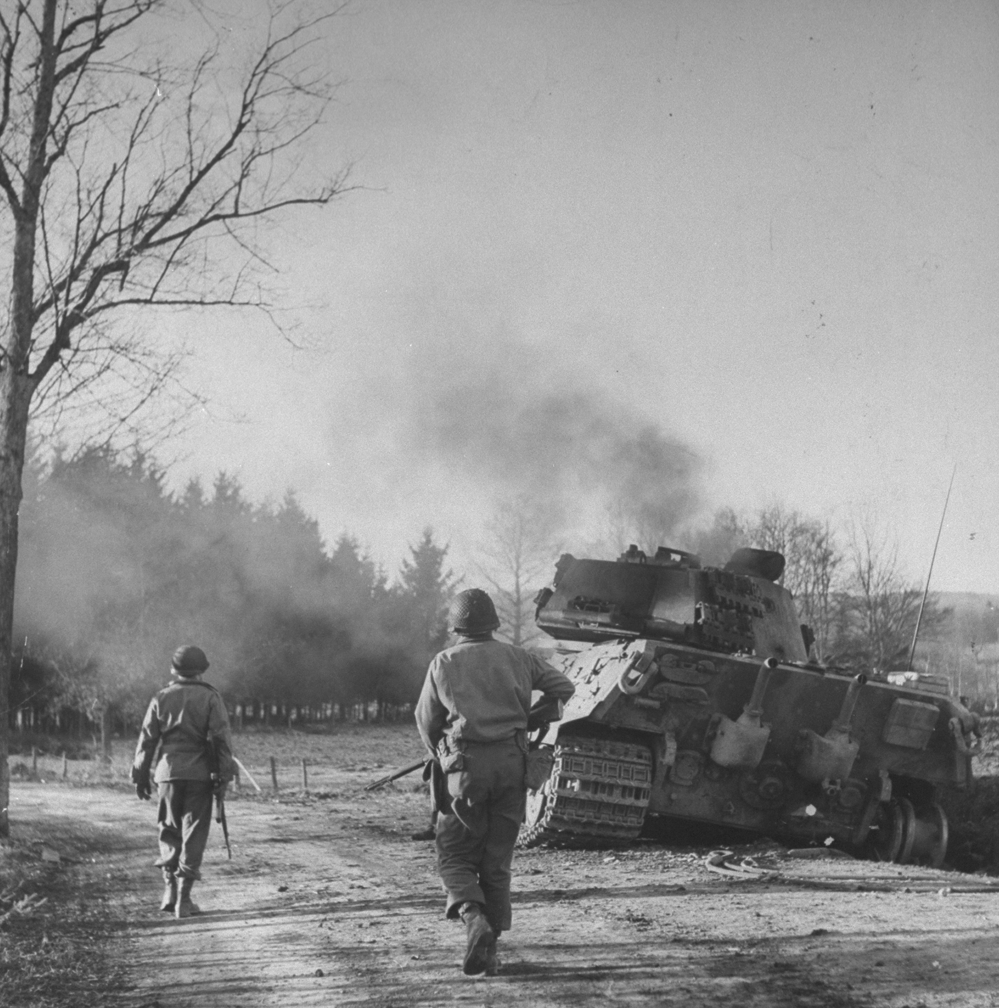 An American patrol moves toward a smoldering German tank, with its crew still inside, Belgium, December 1944.