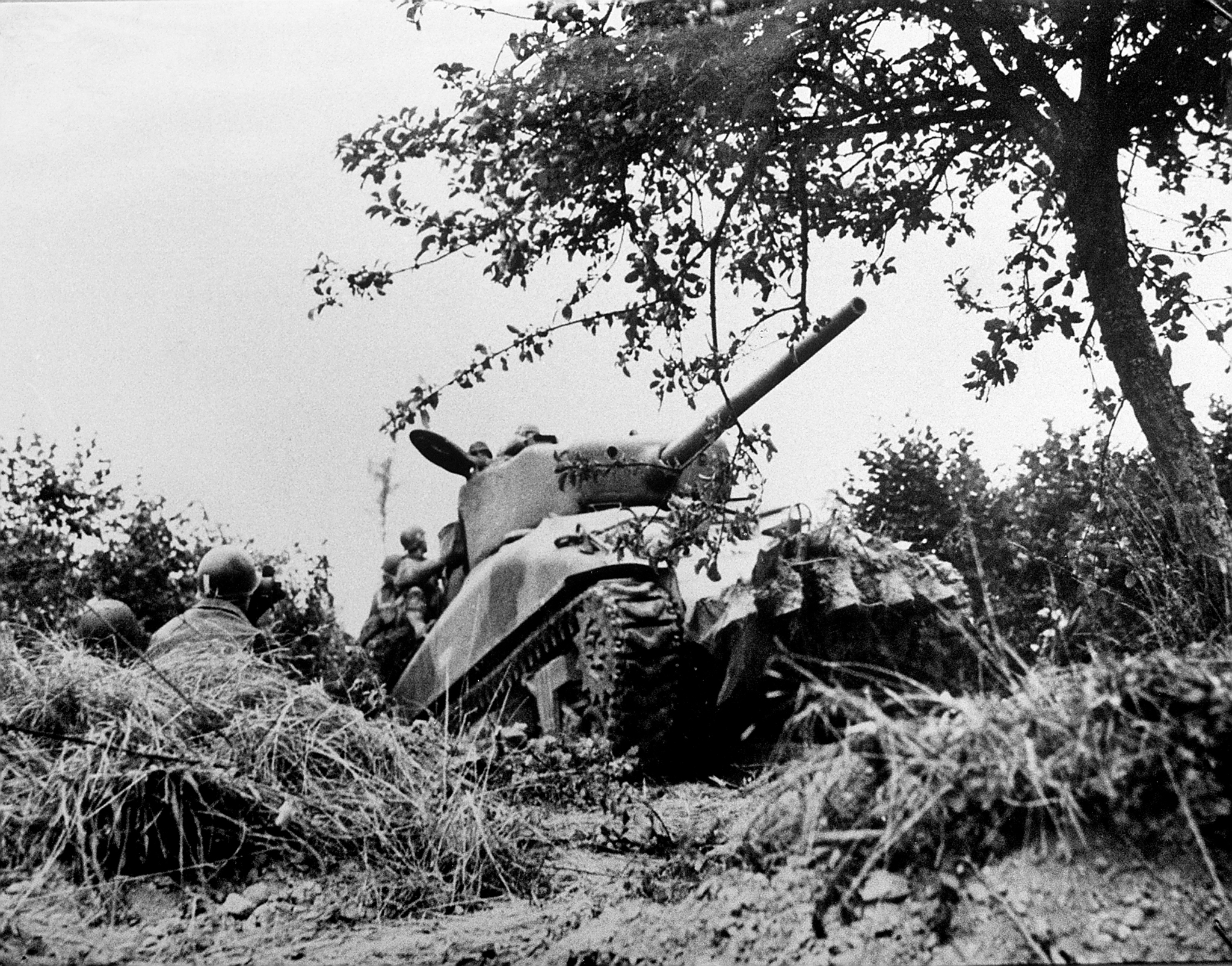 American soldiers and a Sherman tank equipped with a hedgerow-busting plow move forward near the town of Saint-Sauveur-le-Vicomte, 1944.