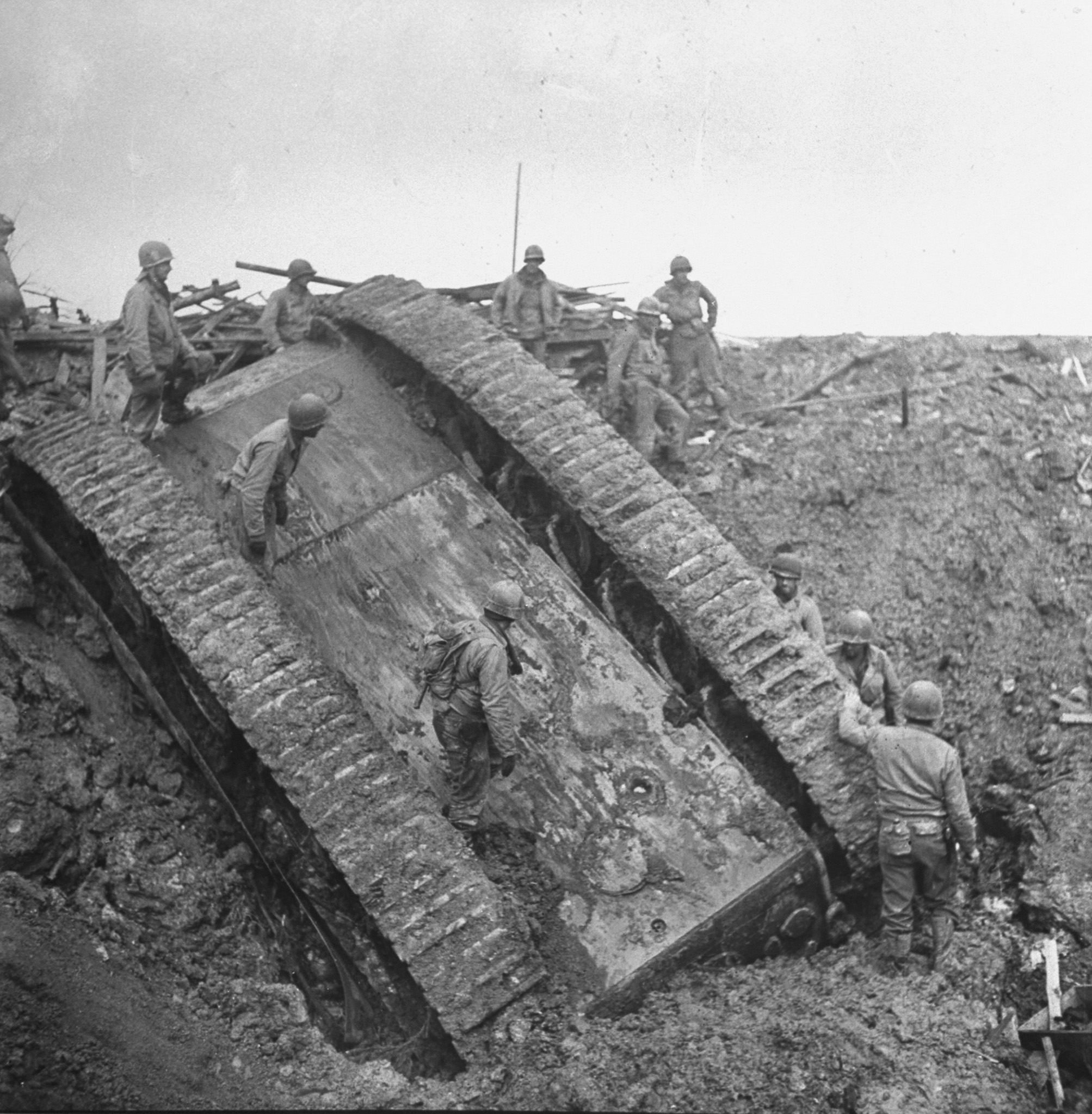 American GIs inspect an overturned German tank, after it toppled into a crater made by a bomb dropped right in front of it by an Allied plane, December 1944.
