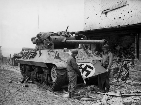 American soldiers of Patton's Third Army roll up a Nazi flag they have taken as a trophy after the capture of Bitburg, February 1945.