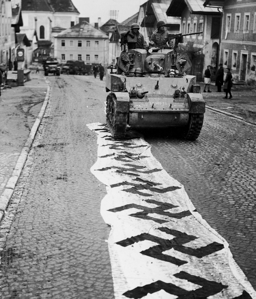 An American tank rolls over a Nazi banner laid out in the street after its crew helped take the town of Lembach, spring 1945.
