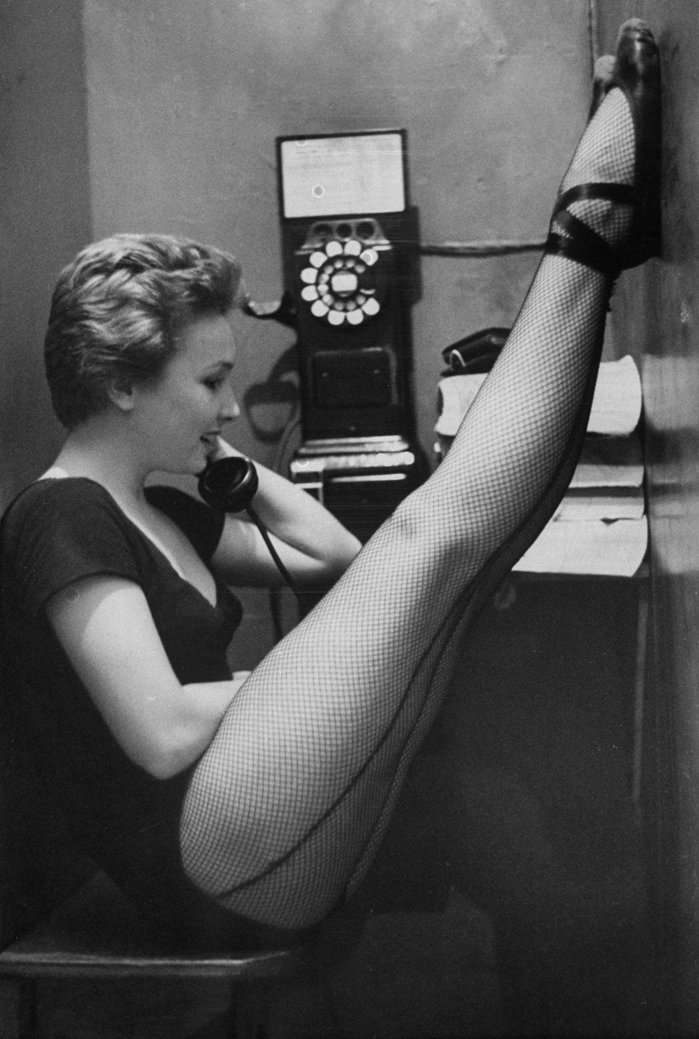 Dancer Mary Ellen Terry talking with her legs up in telephone booth, 1952.