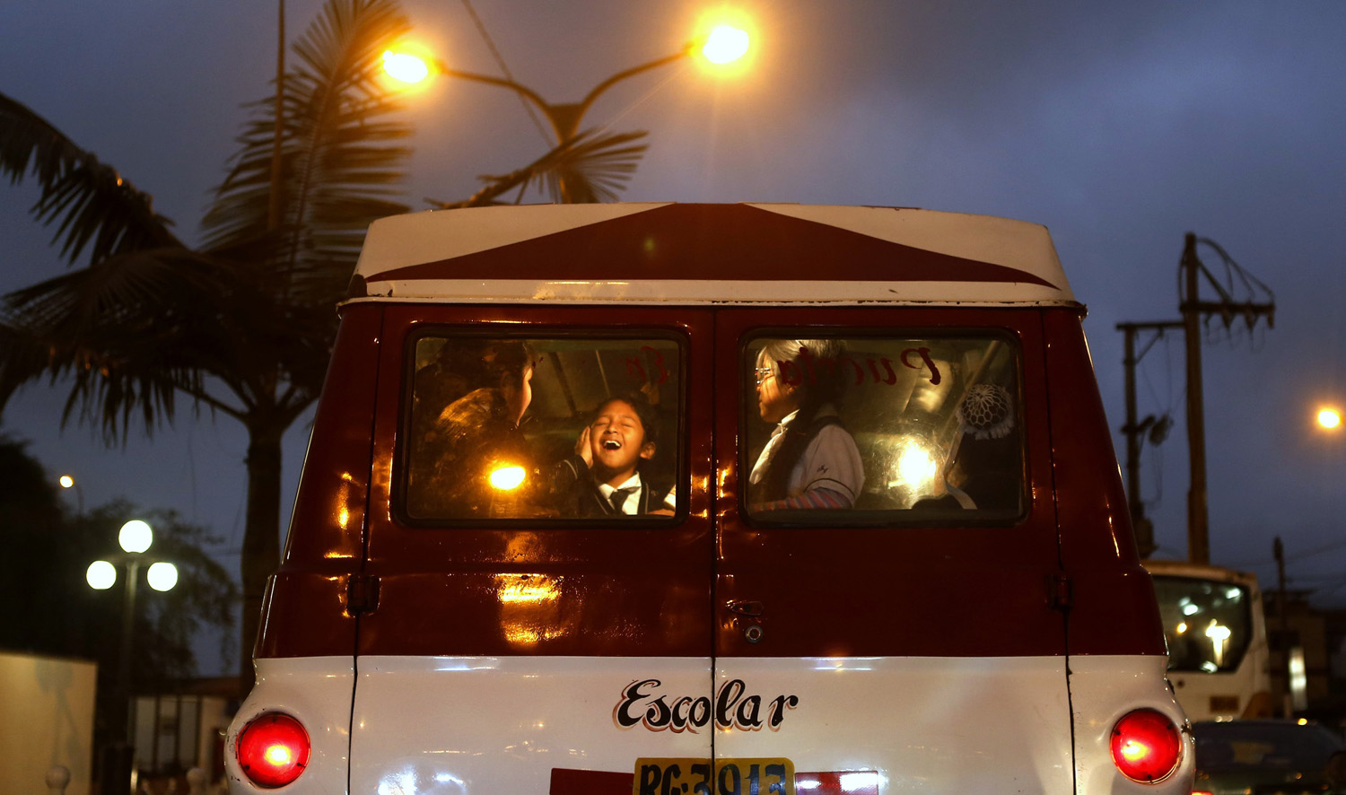 Students are seen through the rear window of a school bus as they travel along a road in Chorrillos