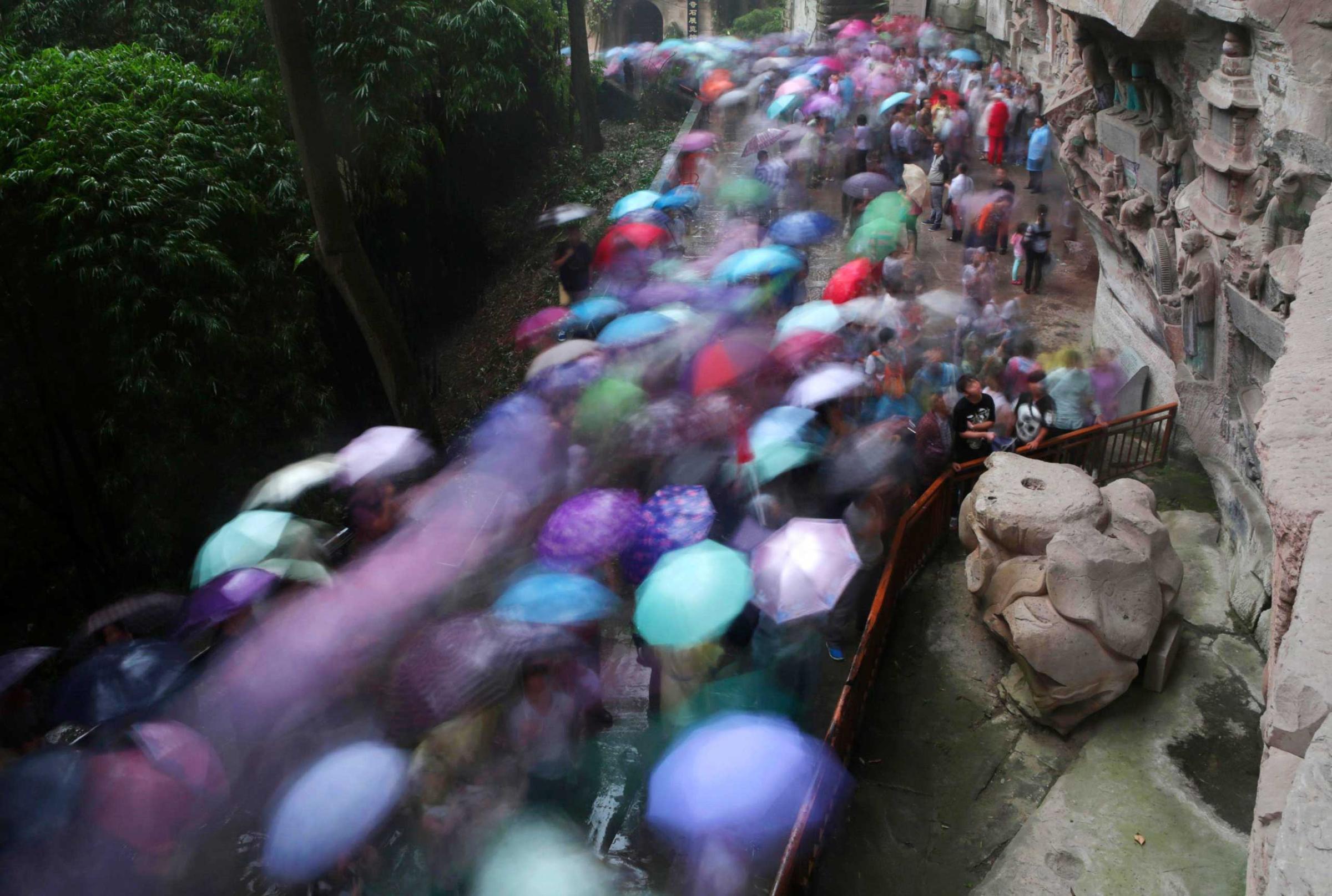 Tourists holding umbrellas crowd visit the stone sculptures at the Baoding Mountain during national day holidays, in Chongqing
