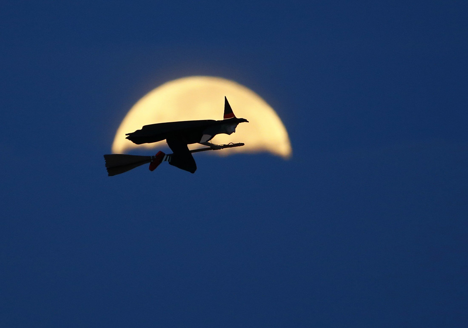 A radio-controlled flying witch flies past a moon setting into clouds along the pacific ocean in Carlsbad, California