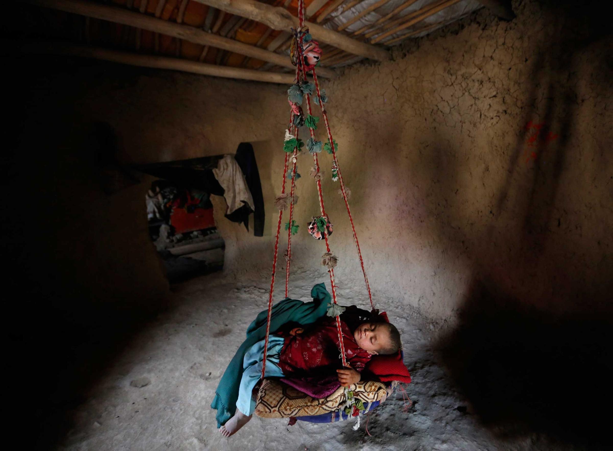 An internally displaced Afghan child sleeps in a hanging cot inside a shelter at a refugee camp in Kabul
