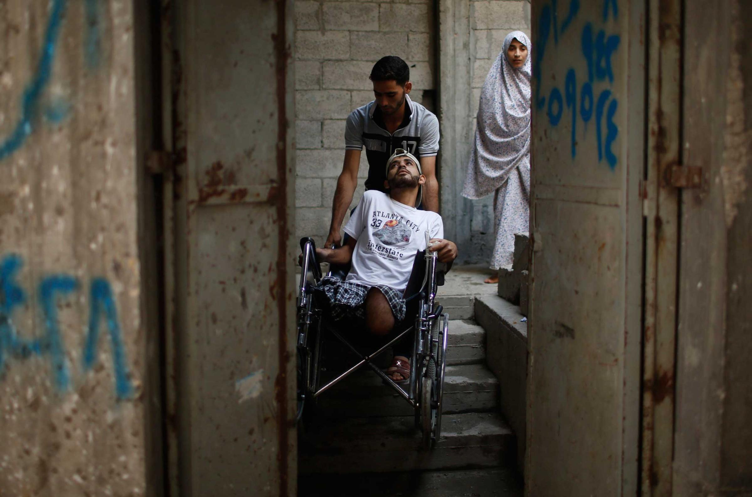 The brother of wheelchair-bound Palestinian Mohammed Abed al-Dayem, 25, pushes him as he enters his house in Beit Lahiya