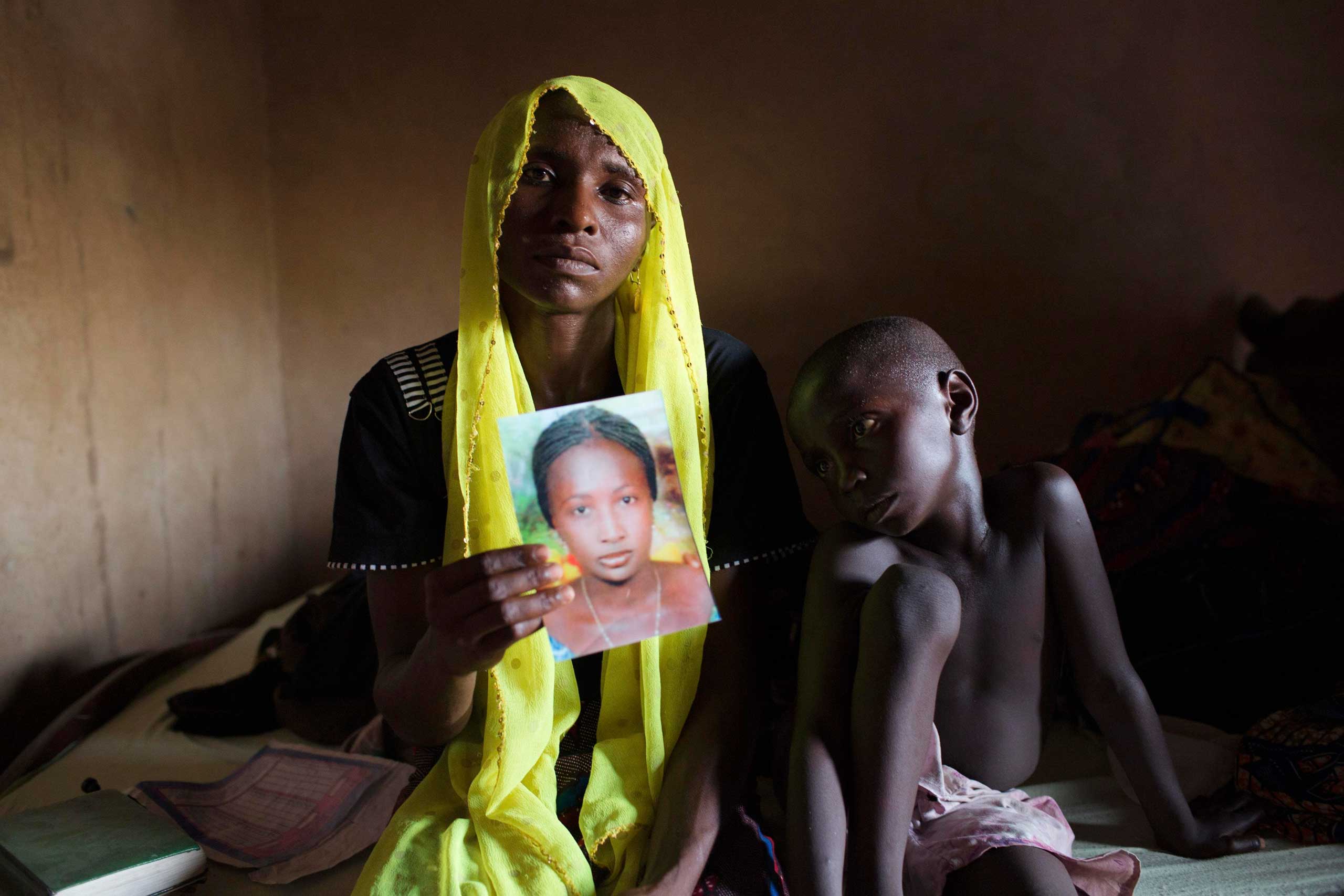 File photo shows Rachel Daniel holding  up a picture of her abducted daughter Rose Daniel as her son Bukar sits beside her at her home in Maiduguri