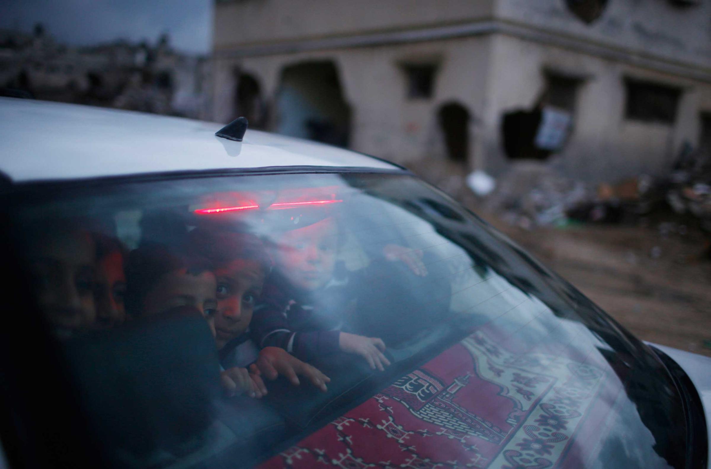 Palestinian children look out of the rear windscreen of a car as they pass damaged houses in the east of Gaza City