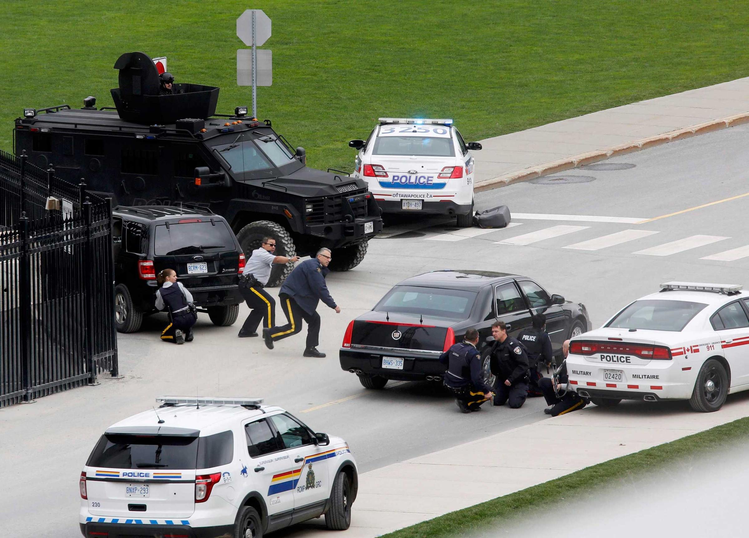 Police officers take cover near Parliament Hilll following a shooting incident in Ottawa
