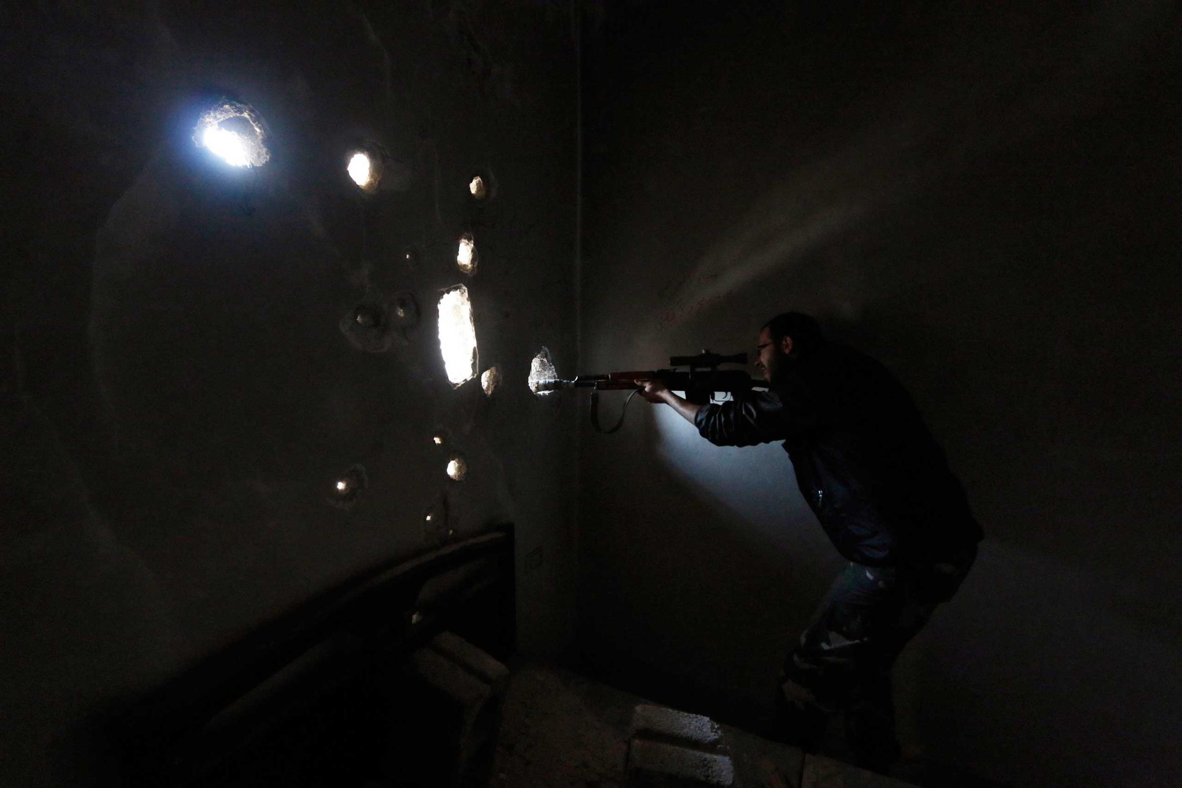 Free Syrian Army fighter carrying a weapon looks through a hole in the wall inside a damaged building on the frontline of Aleppo's Al-Ezaa neighbourhood