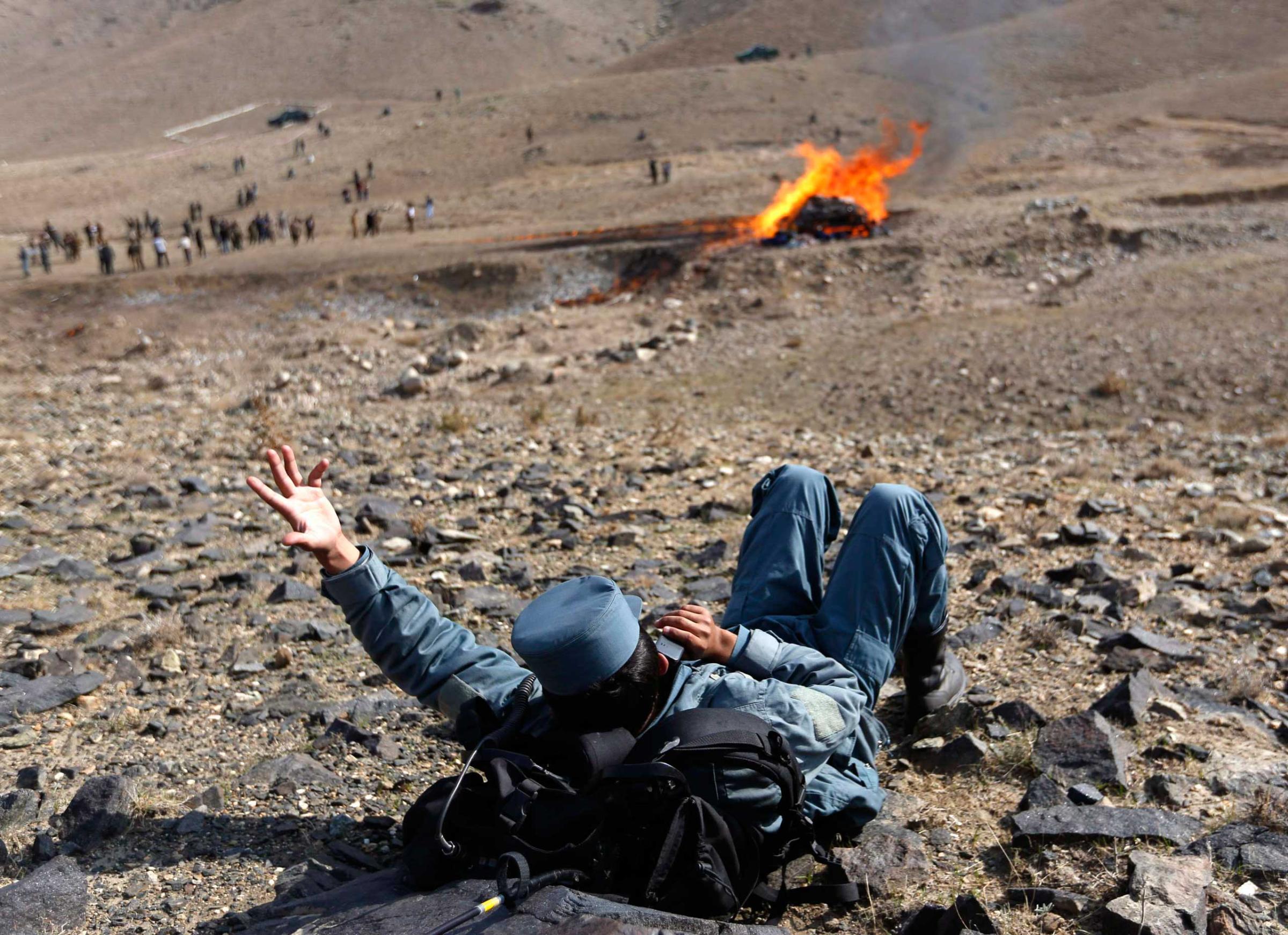An Afghan policeman talks on his phone during the burning of illegal narcotics on the outskirts of Kabul