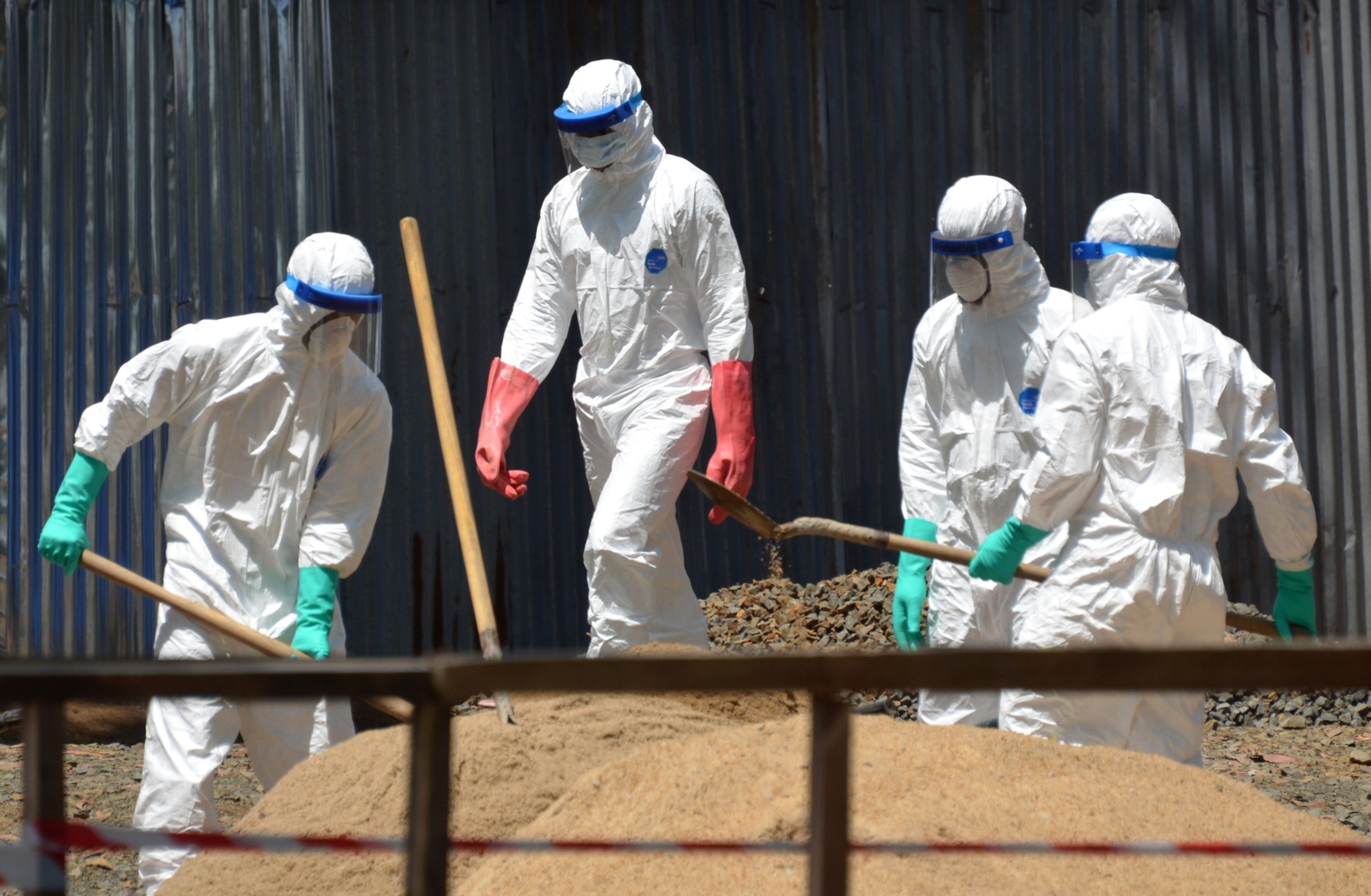Health workers from the Liberian Red Cross wear protective gear as they shovel sand which will be used to absorb fluids emitted from the bodies of Ebola victims in front of the ELWA 2 Ebola management center in Monrovia on October 23, 2014.