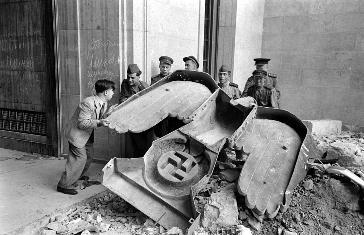 Russian soldiers and a civilian struggle to move a large bronze Nazi Party eagle that once loomed over a doorway of the Reich Chancellery, Berlin, 1945.