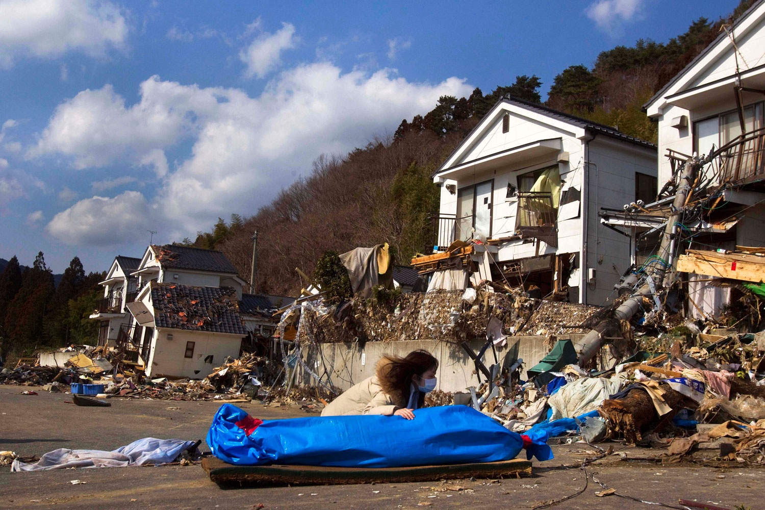 March 19, 2011. Tayo Kitamura, 40, kneels in the street to caress and talk to the wrapped body of her mother Kuniko Kitamura, 69, after Japanese firemen discovered the dead woman inside the ruins of her home in Onagawa, Japan.