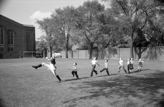 The drum major for the University of Michigan marching band high-steps as children follow suit, 1950.