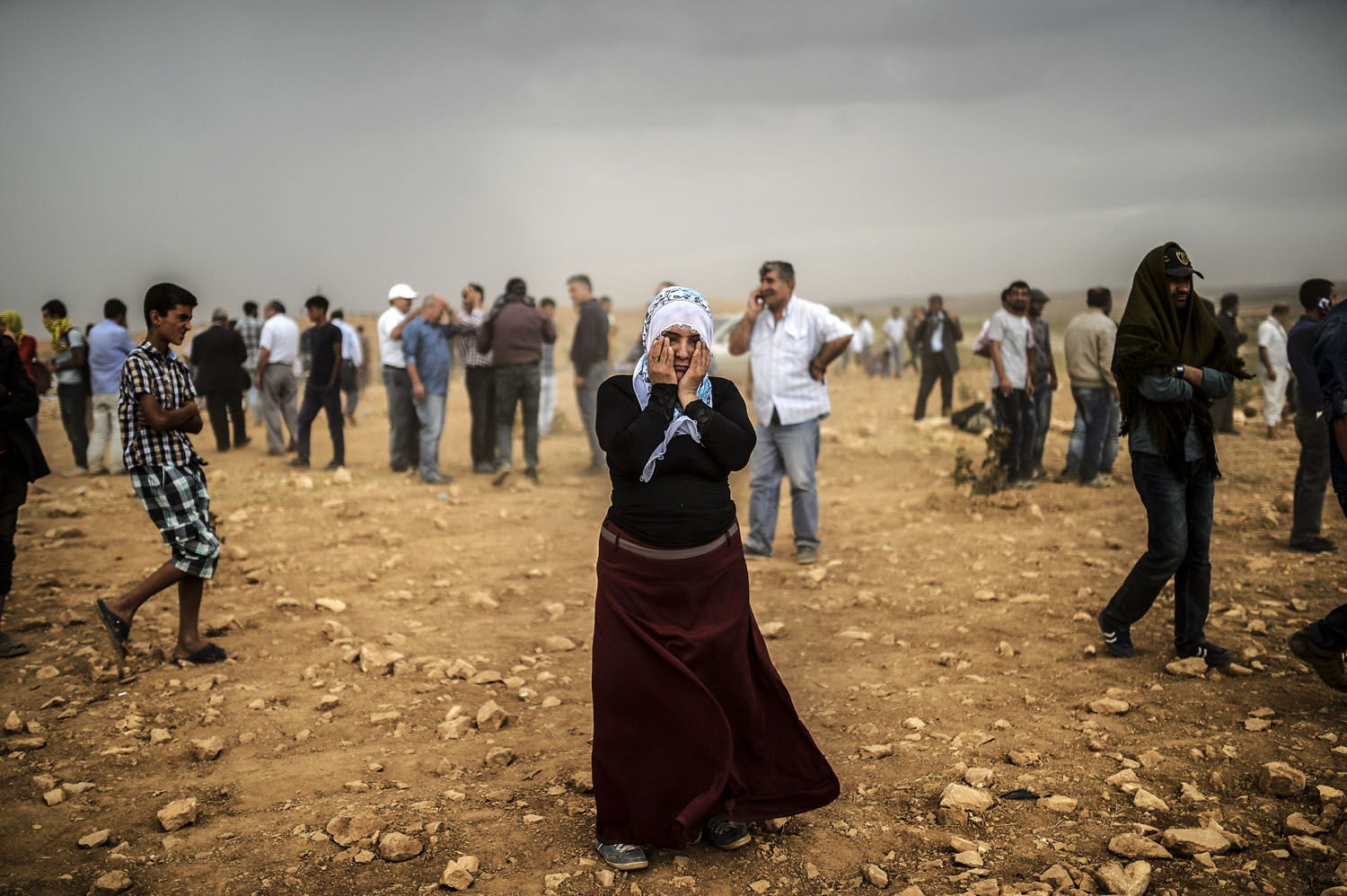 A Syrian Kurdish woman wipes her eyes during a dust storm on a hill where she and others stand watching clashes between jihadists of the Islamic State and Kurdish fighters, at Swedi village some 6 miles west of Suruc in Sanliurfa province, on Sept. 24, 2014.